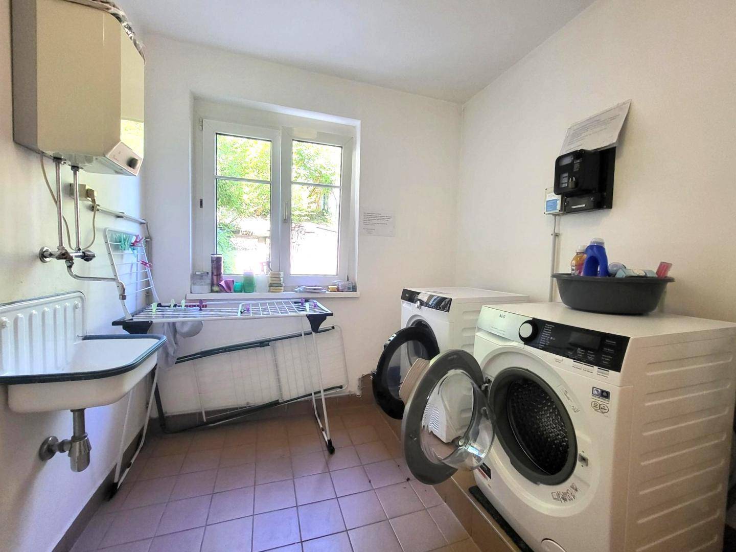 Waschküche mit Waschmaschine, Trockner, Waschbecken und Fenster.