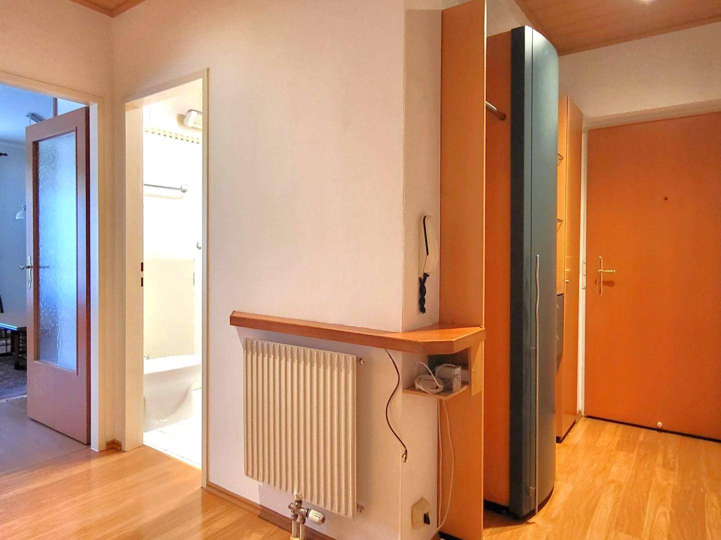 Flur mit Holzboden, Heizkörper und Blick in ein angrenzendes Badezimmer.