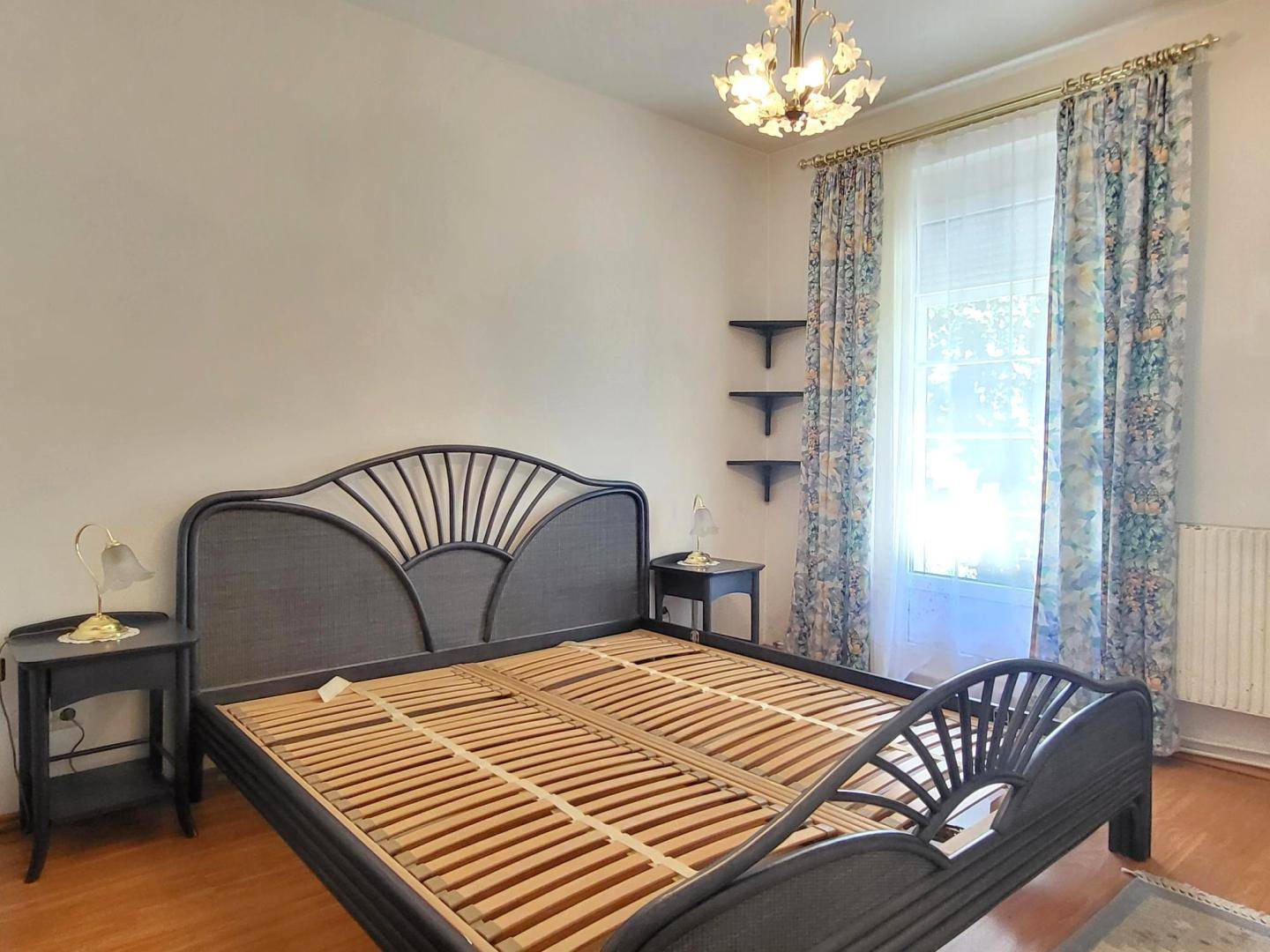 Schlafzimmer mit Doppelbett, Nachttischen und Fenster mit floralen Vorhängen.