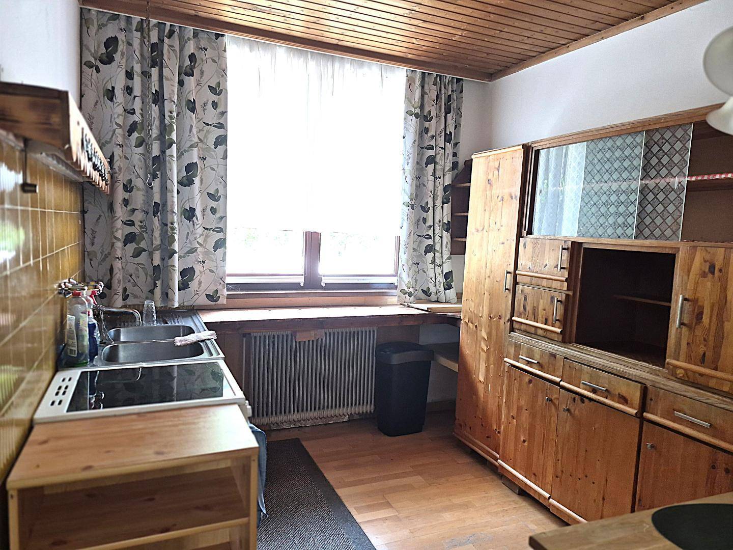 Rustikale Küche mit Holzmöbeln, Holzbalkendecke und einem Fenster mit floralen Vorhängen.