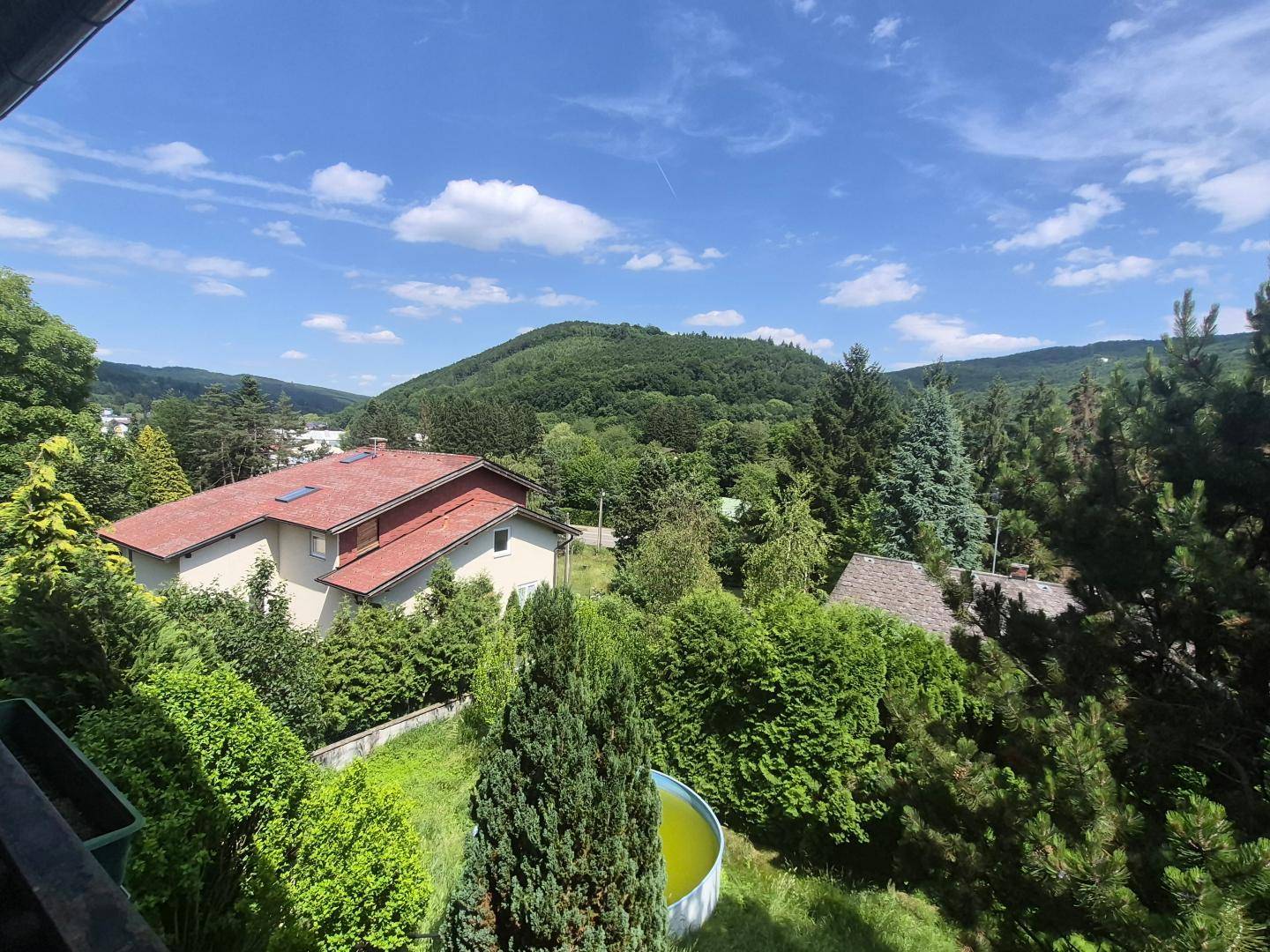 Weitläufiger Blick über grüne Hügel und bewaldete Landschaft unter blauem Himmel mit Wolken.
