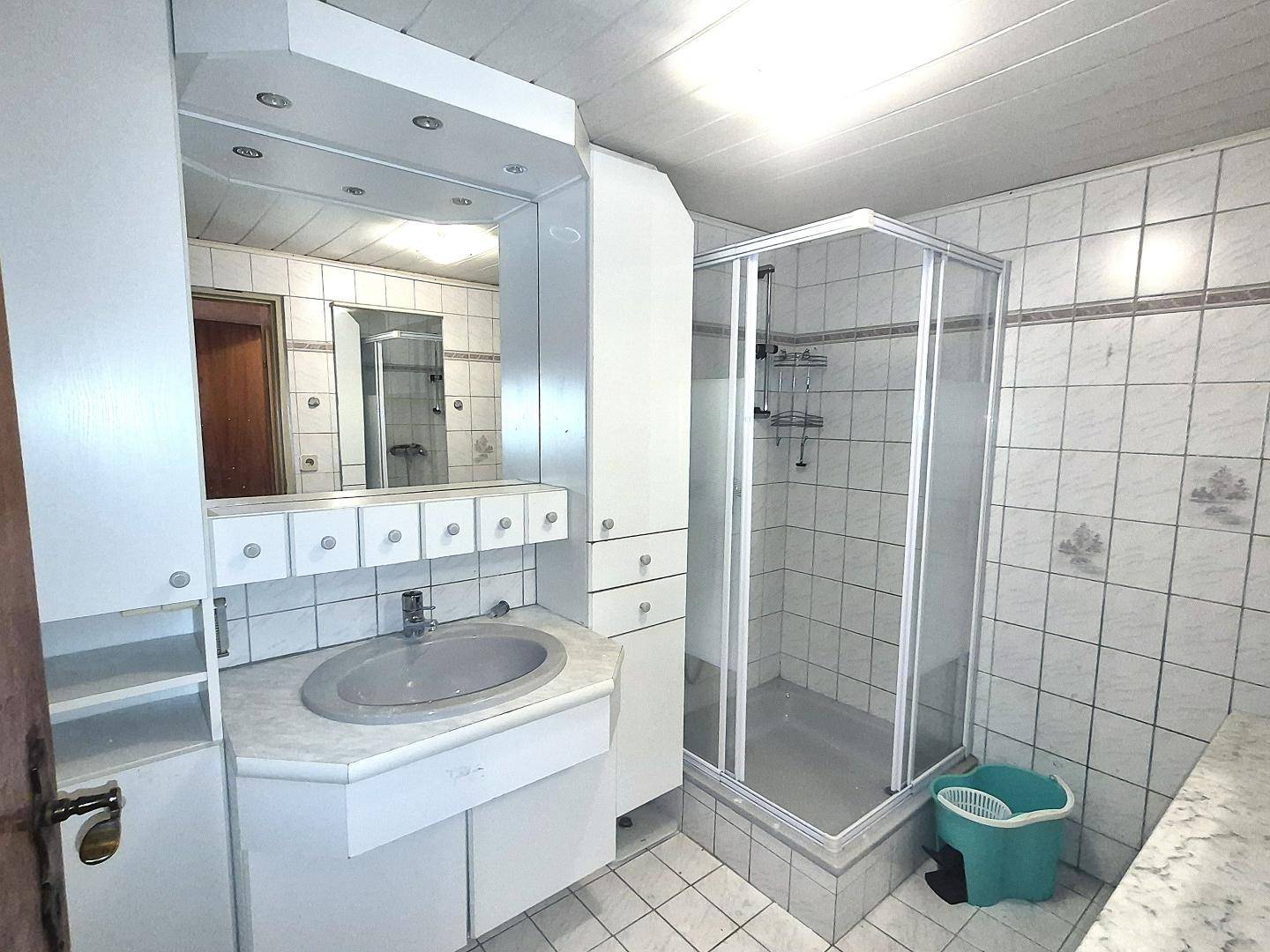 Badezimmer mit Duschkabine, Waschbecken und Spiegelschrank, in hellen Fliesen gehalten.