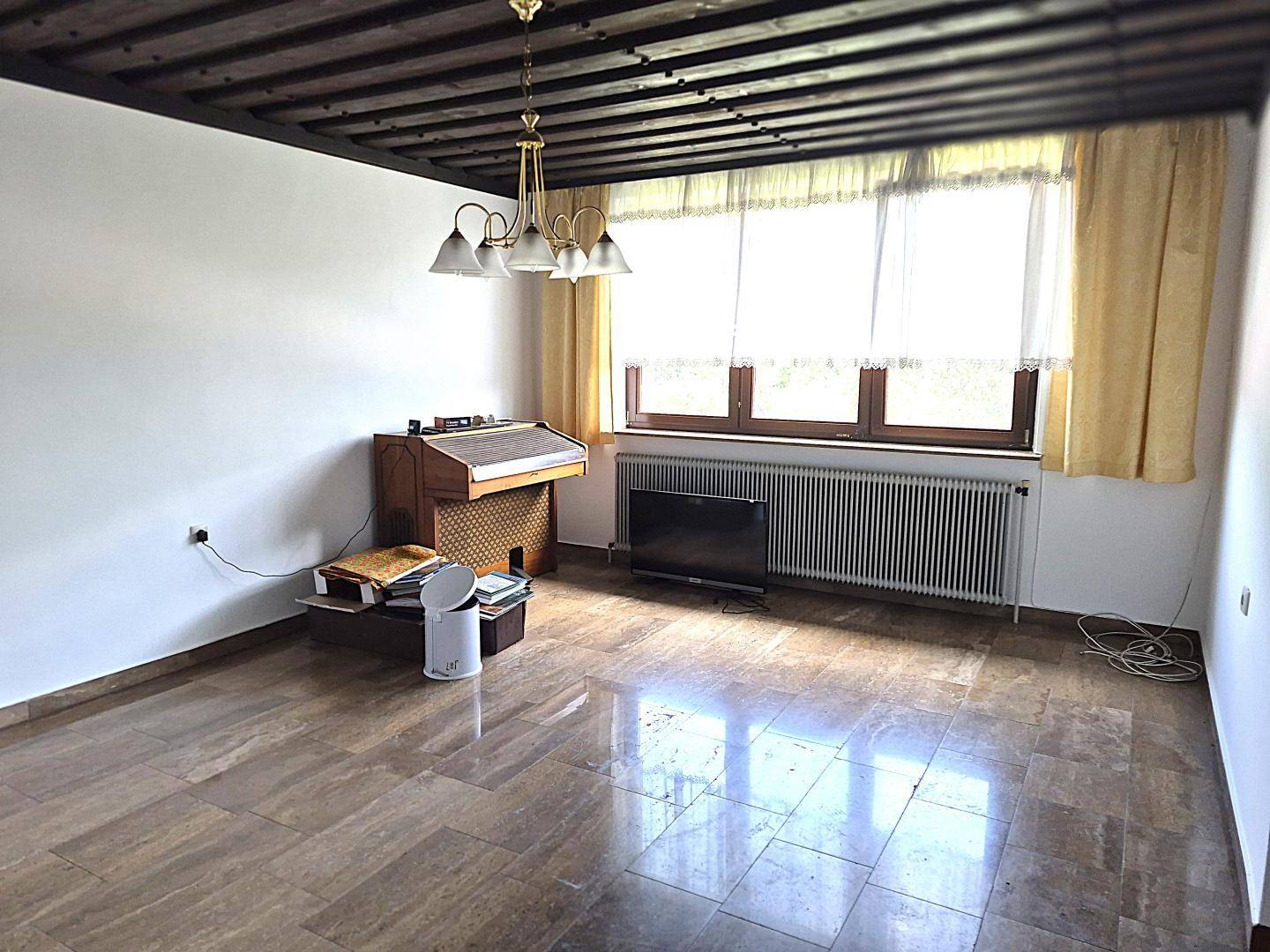 Wohnzimmer mit freiliegenden Holzbalken, großem Fenster und glänzendem Marmorboden.