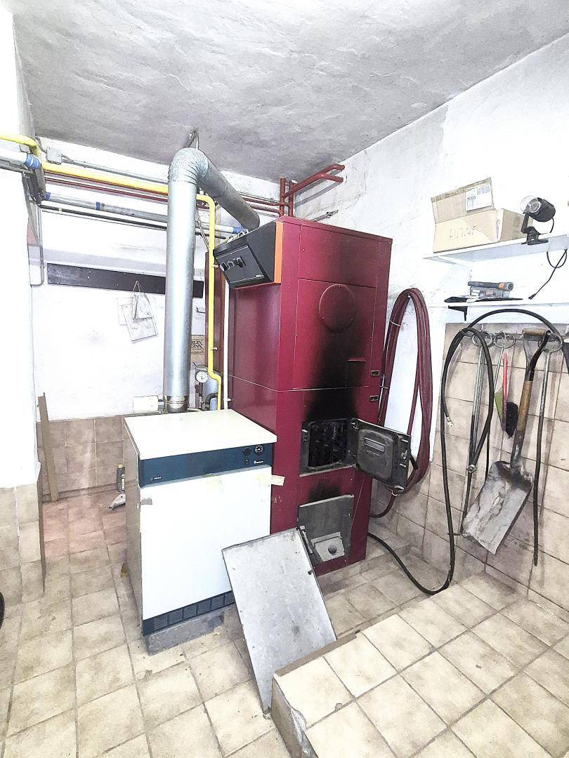 Heizungsraum mit einem großen roten Heizkessel, Rohren und Werkzeugen an der Wand.