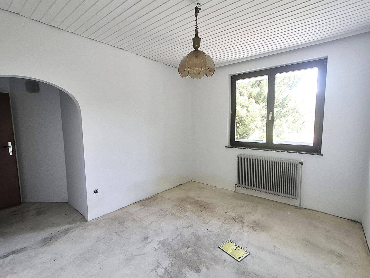 Leeres Zimmer mit weiß gestrichenen Wänden, einem Fenster und einem einfachen Betonboden.
