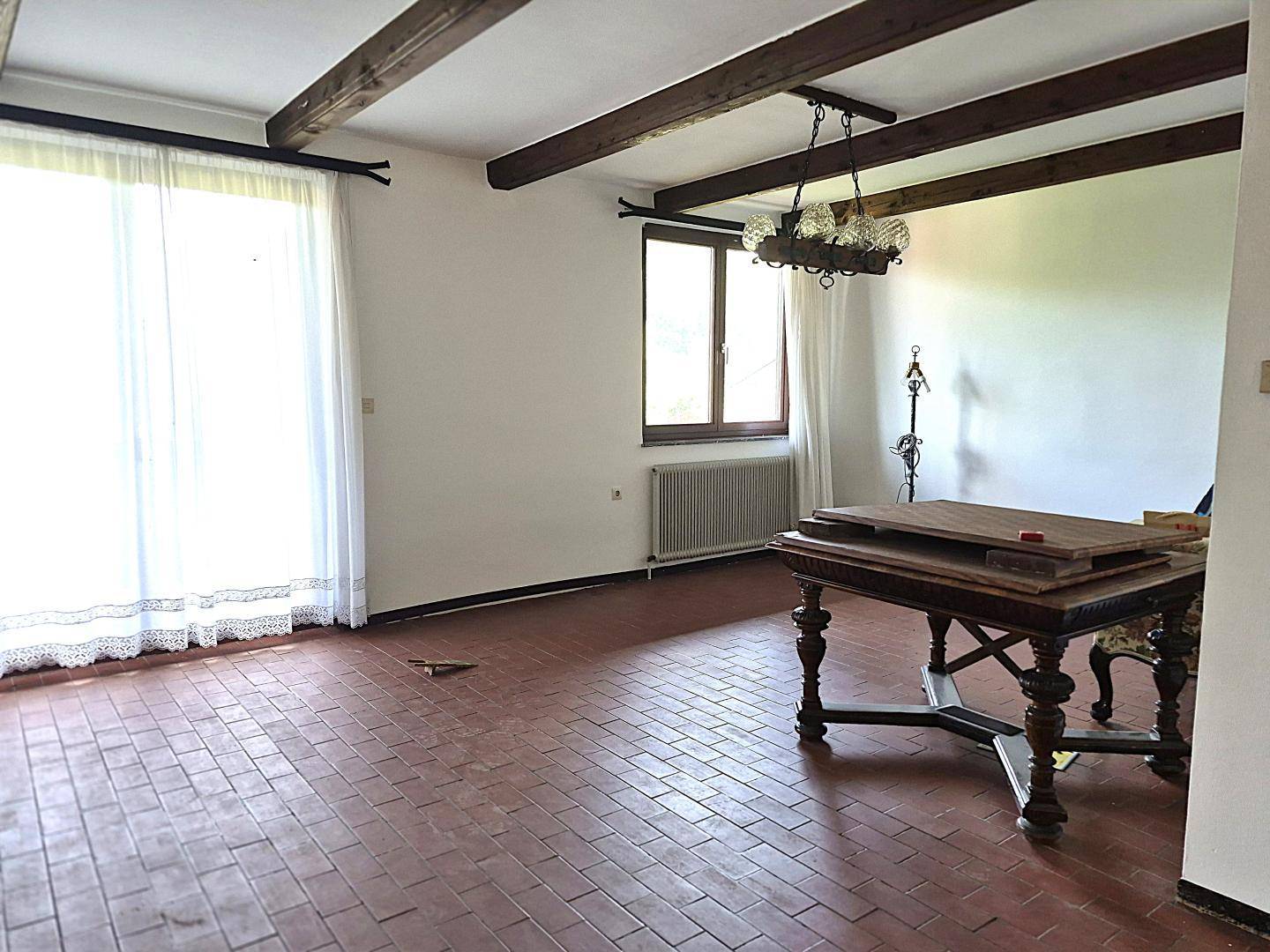 Geräumiges Wohnzimmer mit Terrakotta-Fliesenboden, freiliegenden Holzbalken und Zugang zum Außenbereich.