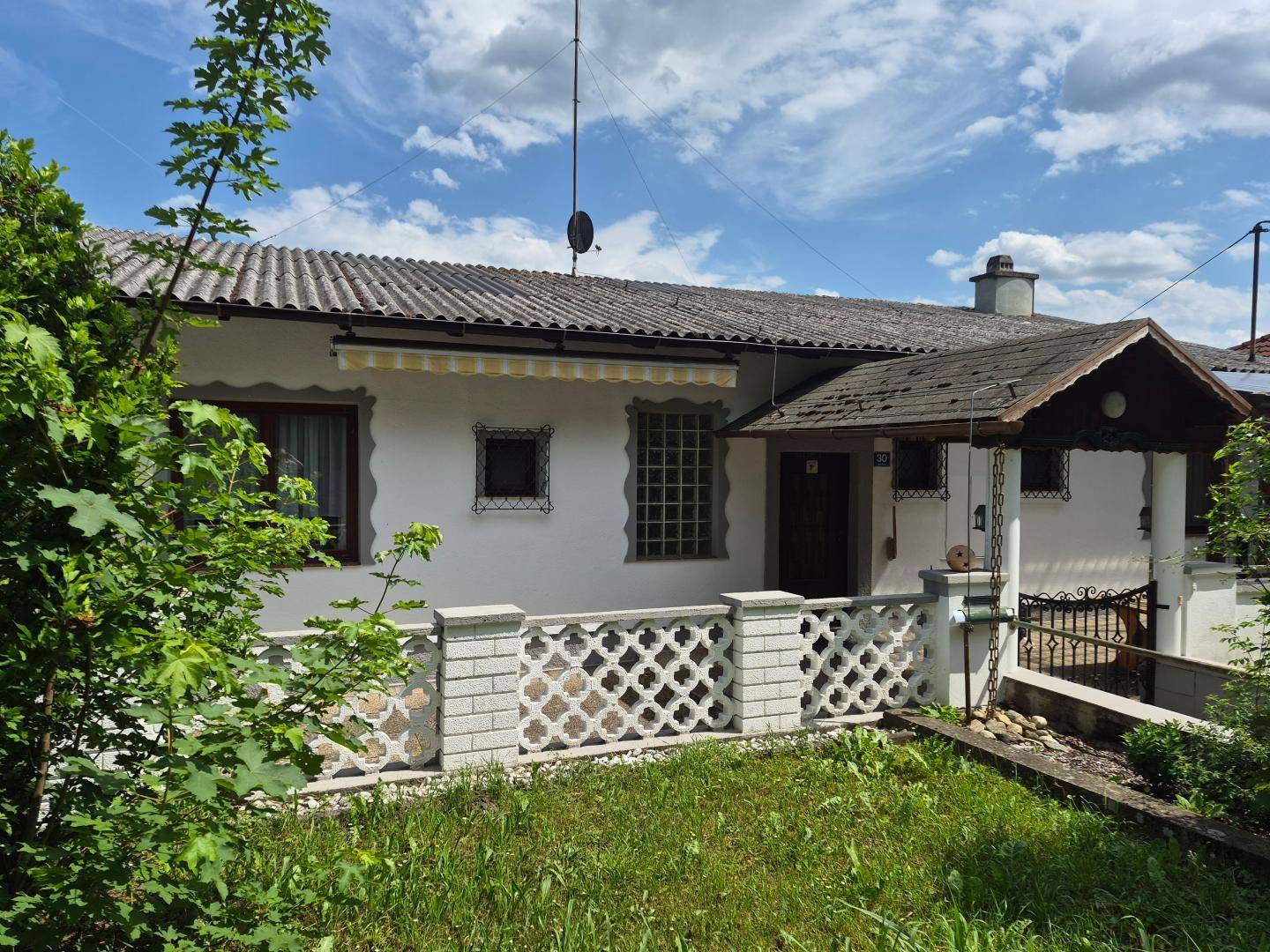 Vorderansicht eines Einfamilienhauses mit weißer Fassade, Vordach und einem kleinen Vorgarten.