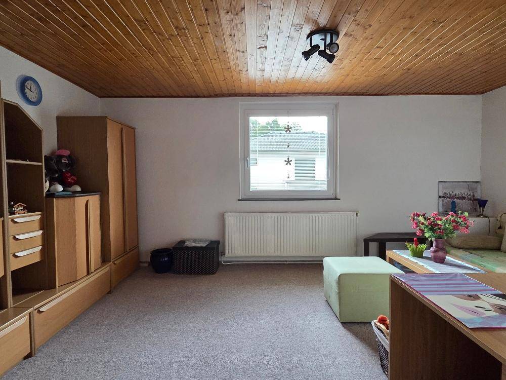 Gemütliches Zimmer mit Holzdecke, Teppichboden und Fenster mit Blick nach draußen.