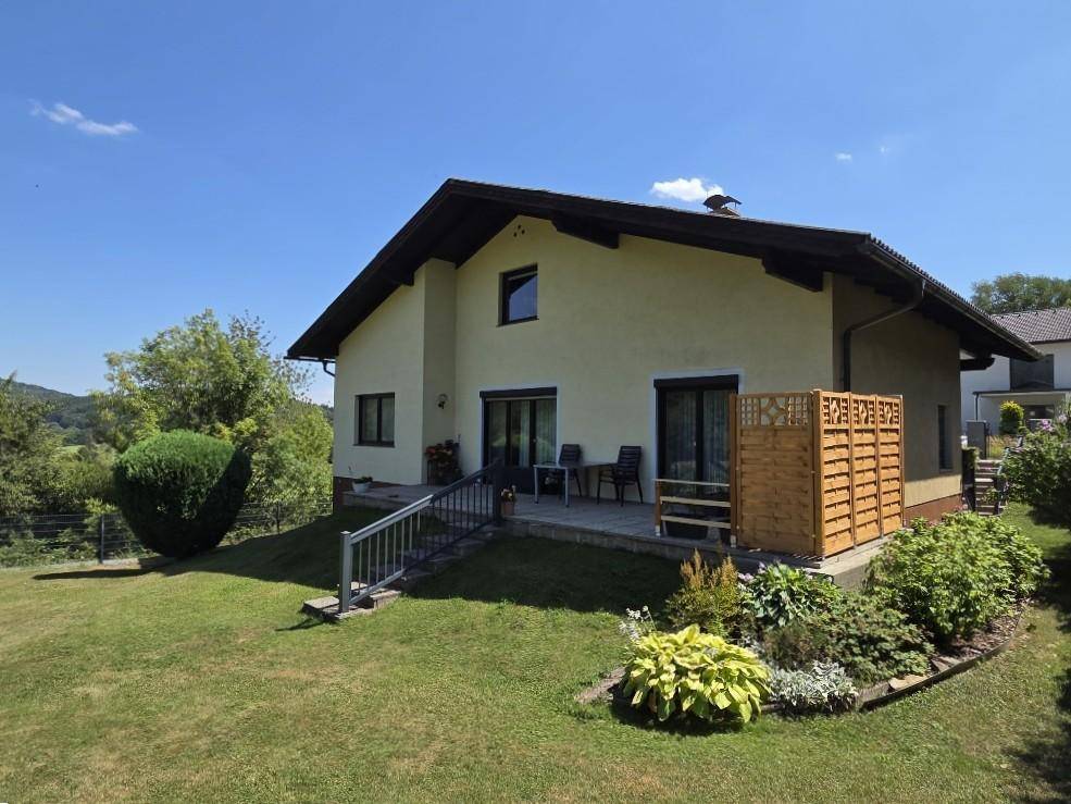 Hinteransicht des Hauses mit einer gepflasterten Terrasse und Zugang zum weitläufigen Garten.