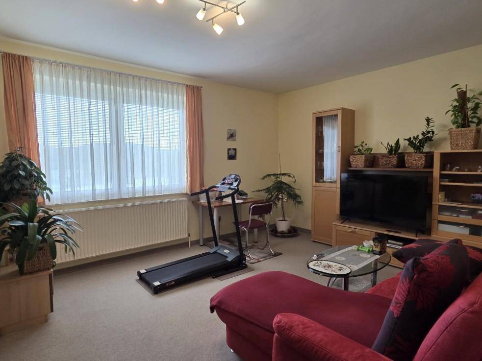 Helles Wohnzimmer mit Teppichboden, großem Fenster und Zugang zum Balkon oder Garten.
