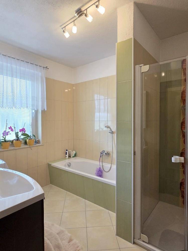 Badezimmer mit Badewanne, Duschkabine, Fliesen und Fenster für Tageslicht.