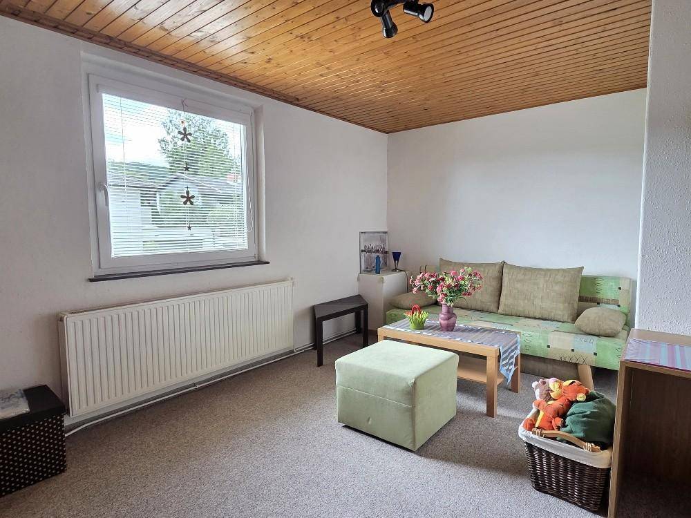 Helles Zimmer mit Holzdecke, Teppichboden und einem Sofa, ideal als Gästezimmer.