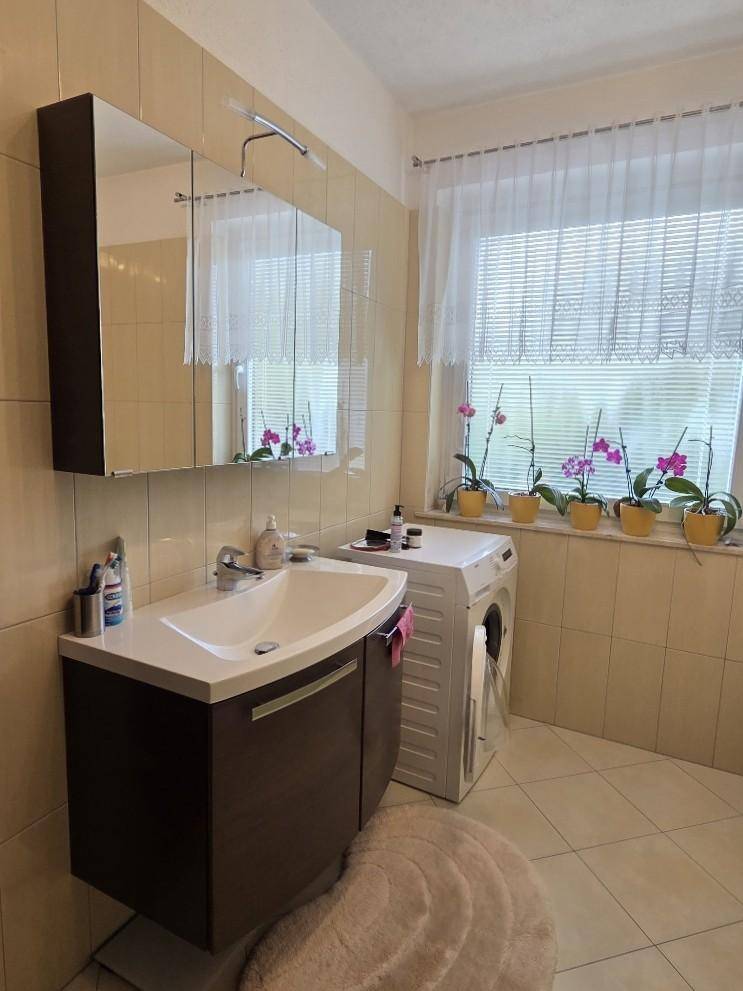 Helles Badezimmer mit Waschbecken, Spiegelschrank, Waschmaschine und Fenster.