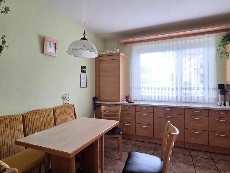 Gemütliche Wohnküche mit Essecke, Holzmöbeln und hellem Fensterbereich.