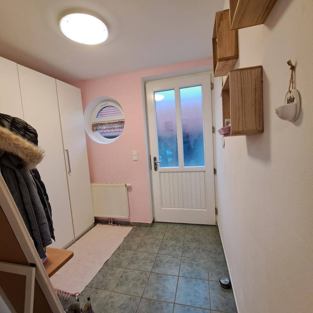 Eingangsbereich mit rosa Wand, runden Fenster und Fliesenboden, bietet praktischen Stauraum.