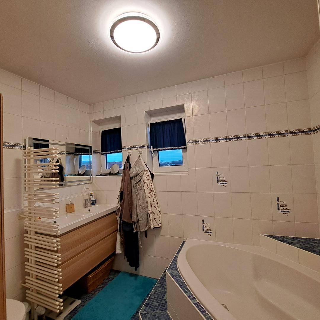 Gefliestes Badezimmer mit Badewanne, Waschbecken und beheiztem Handtuchhalter, bietet Komfort.