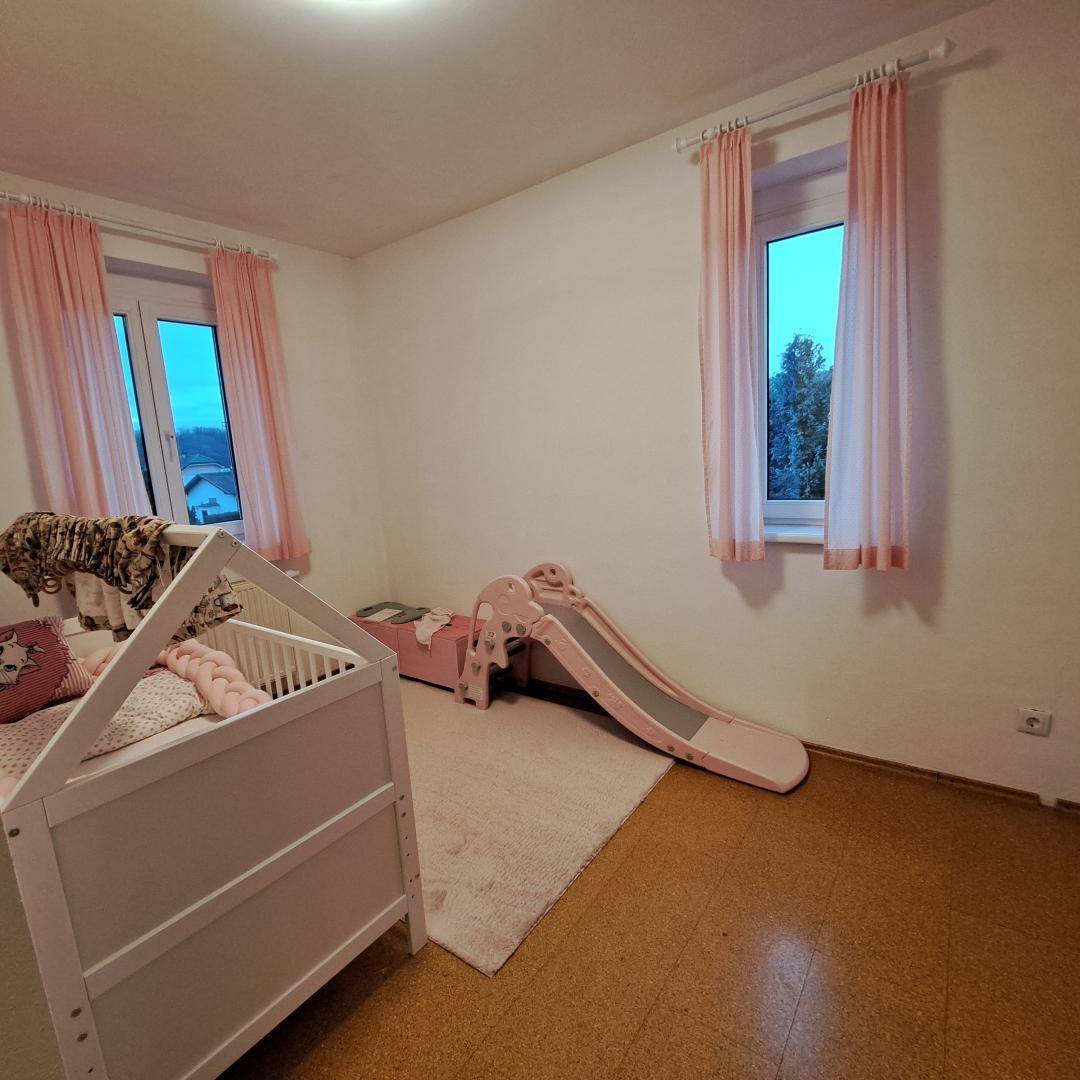 Kinderzimmer mit Babybett, Rutsche und rosa Vorhängen, ideal für kleine Kinder.