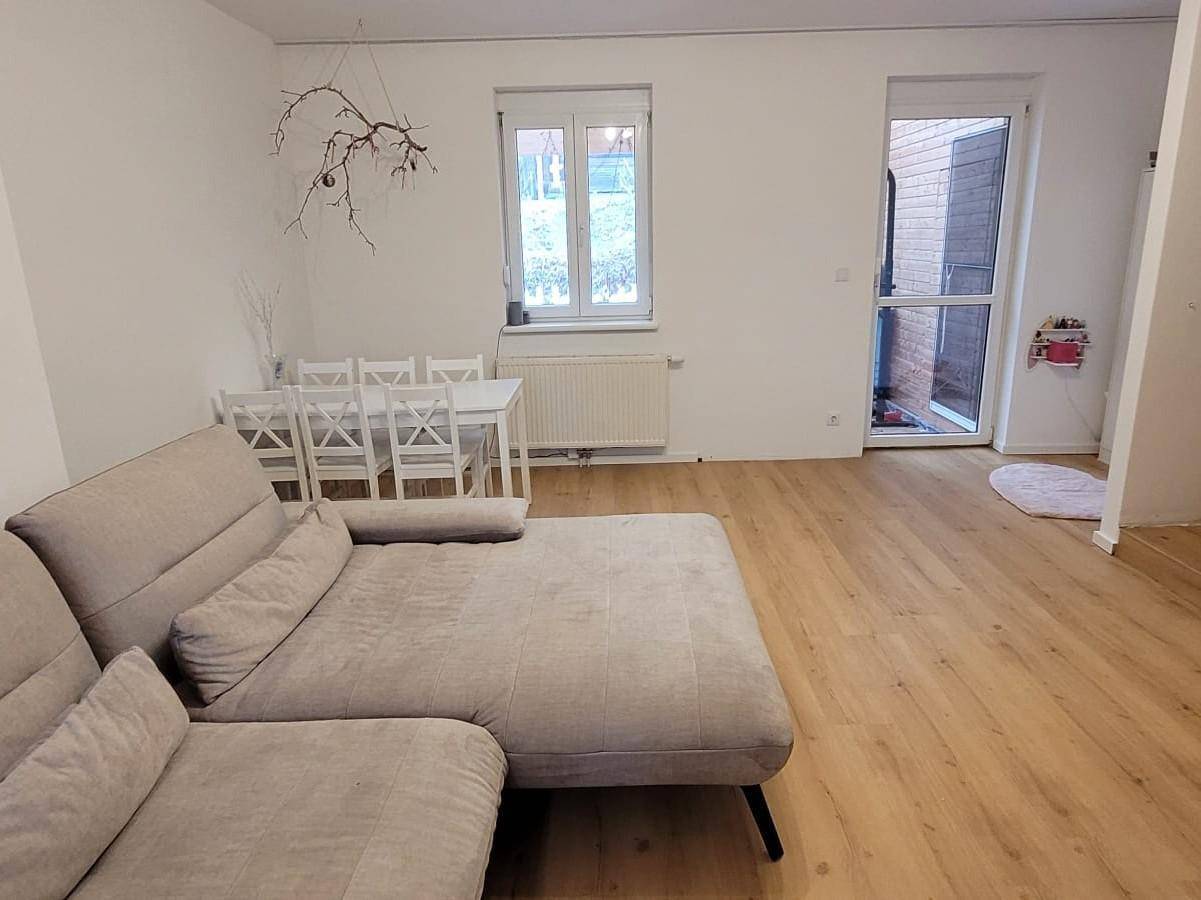 Gemütlicher Wohn-Essbereich mit hellem Holzboden, Sofa und Esstisch, mit Zugang zum Außenbereich.