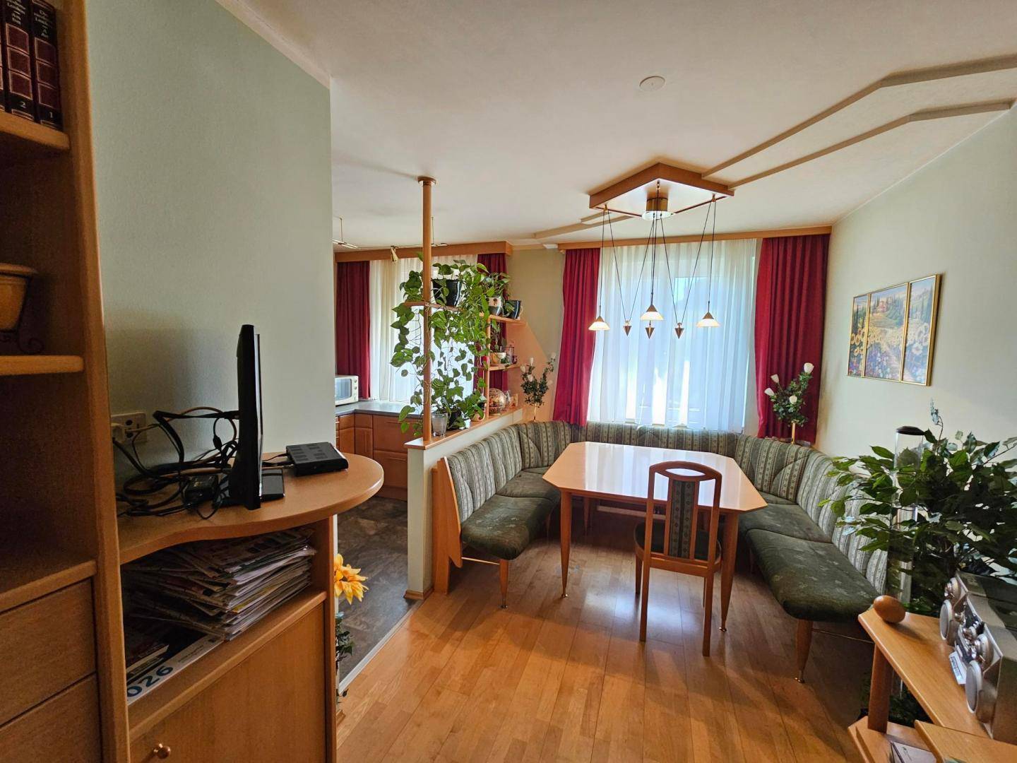 Heller Essbereich mit Eckbank und Holztisch, offen zur Küche mit vielen Pflanzen.