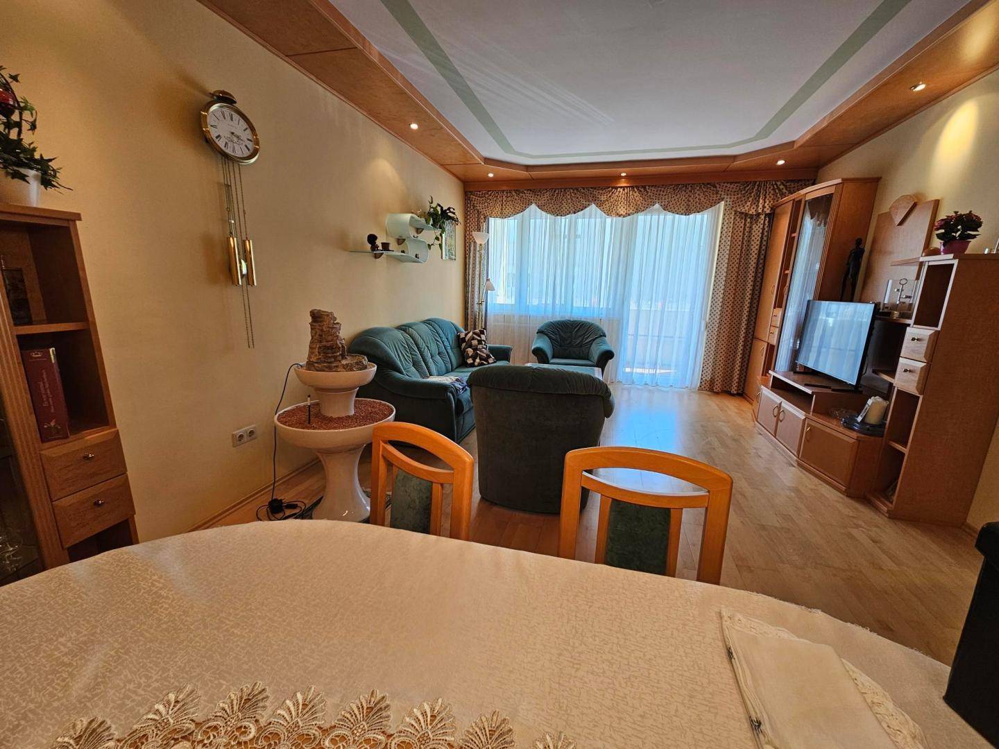 Gemütliches Wohnzimmer mit traditionellen Möbeln, einem großen Uhrwerk und Blick ins Grüne.