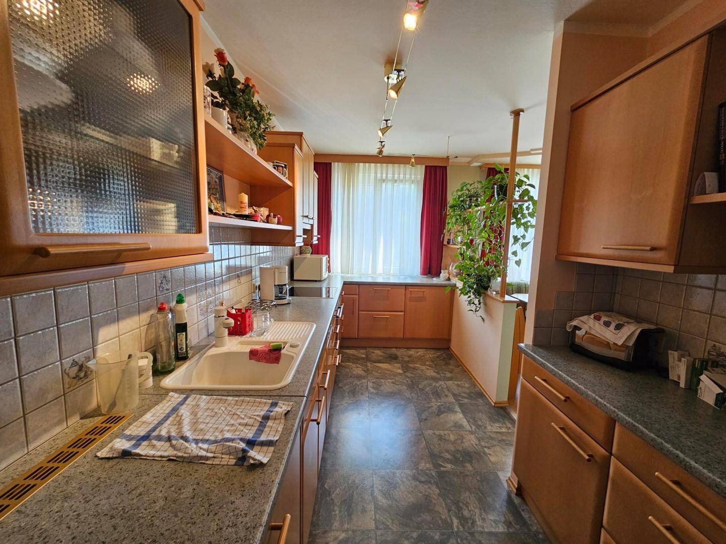 Funktionale Küche mit Holzschränken, grauen Fliesen und dunklem Bodenbelag.