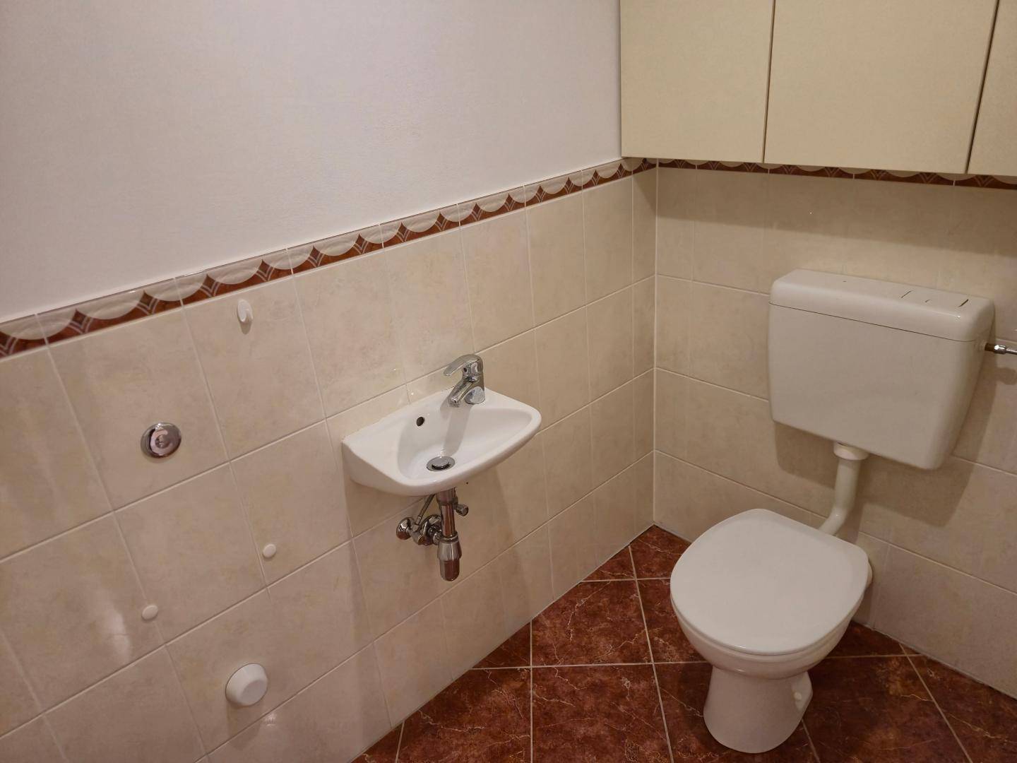Kleines Gäste-WC mit WC, Waschbecken und Fliesenboden in warmen Farbtönen.