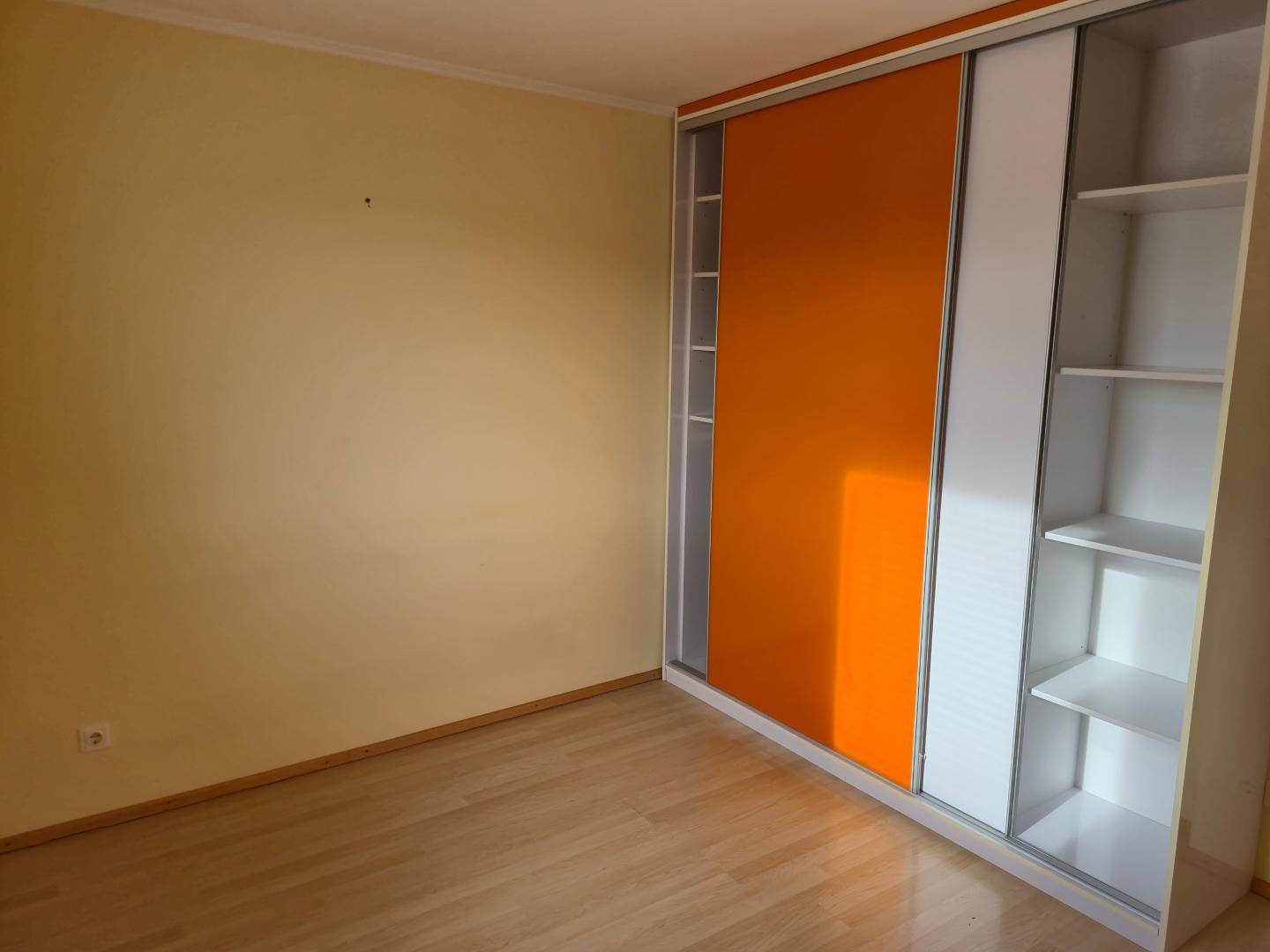Schlafzimmer mit hellem Parkettboden und einem modernen Einbauschrank mit orangefarbenen Schiebetüren.