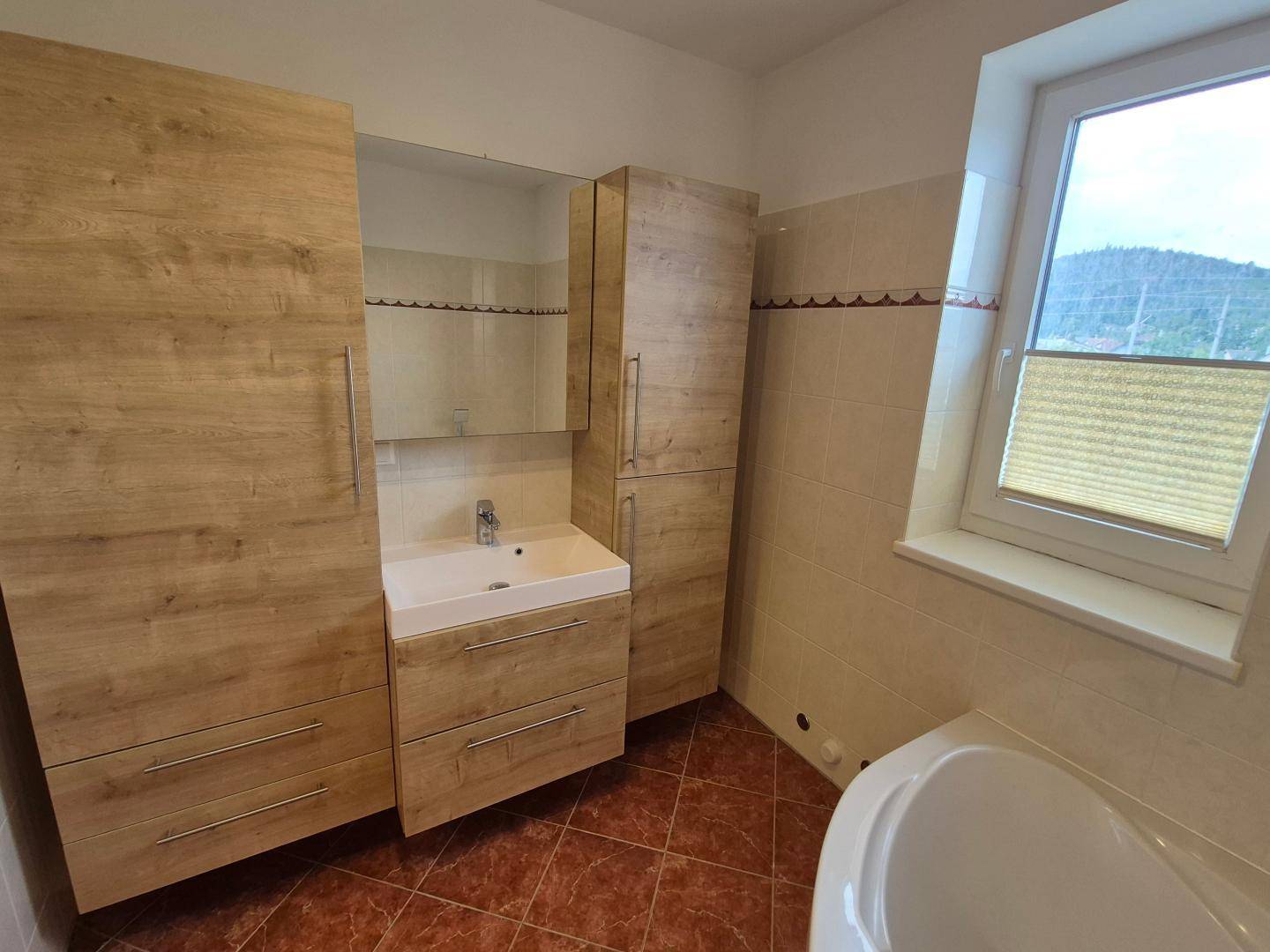 Badezimmer mit Holzwaschtisch, Spiegelschrank, Eckbadewanne und Fenster für natürliche Belüftung.