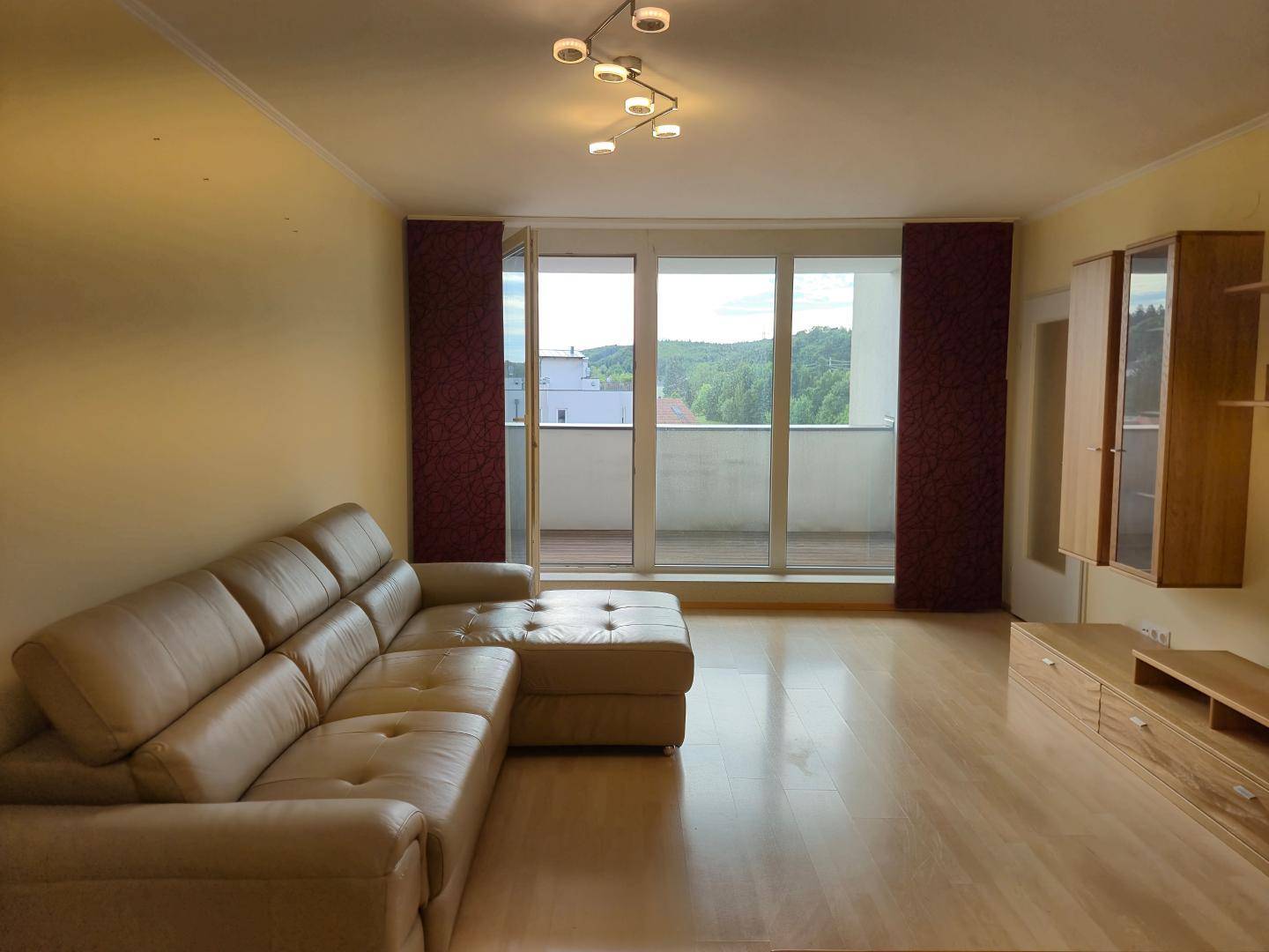 Gemütliches Wohnzimmer mit beiger Eckcouch und großem Fenster mit Zugang zum Balkon.