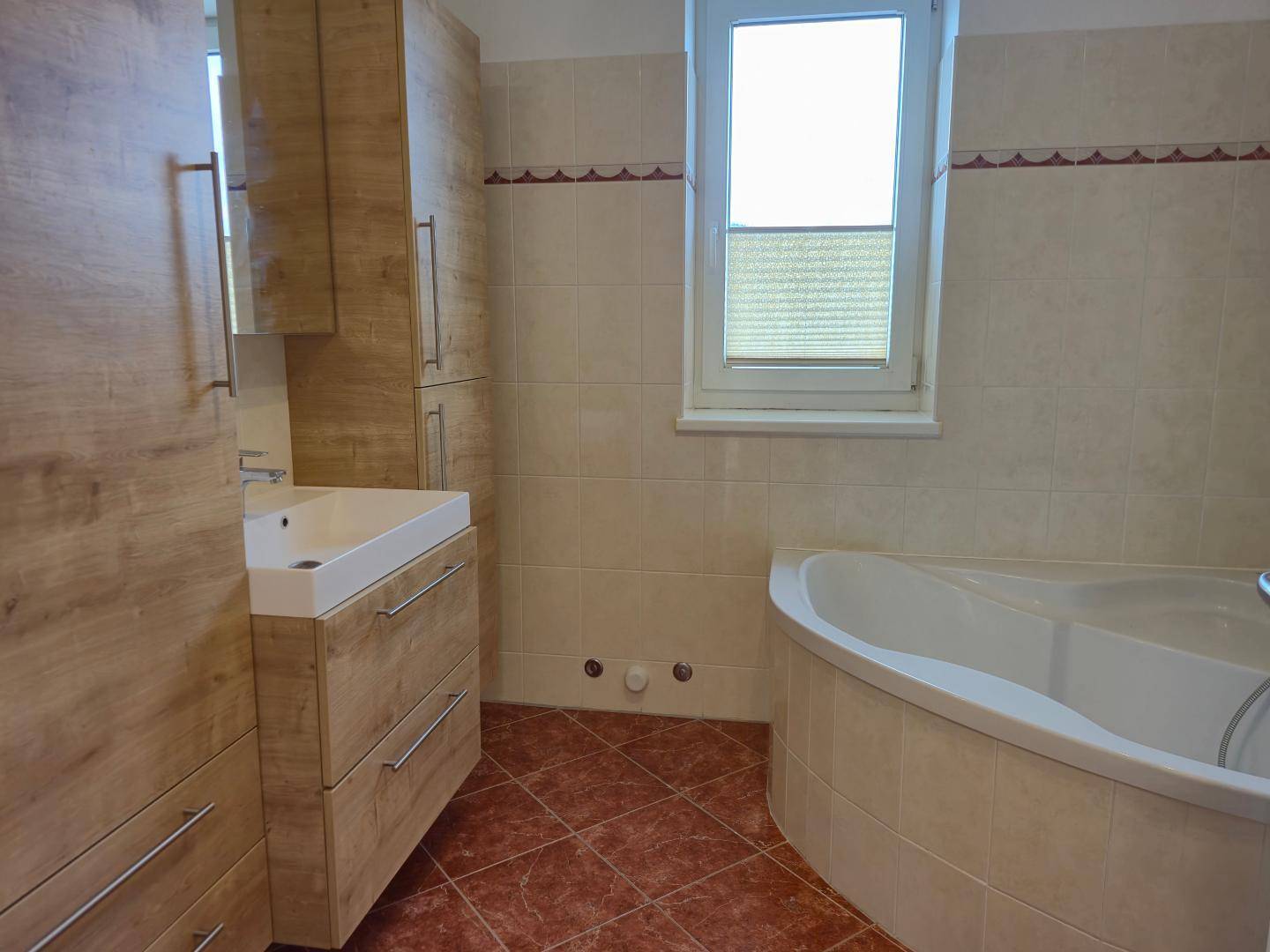 Helles Badezimmer mit Eckbadewanne, modernem Waschtisch und Holzschränken.