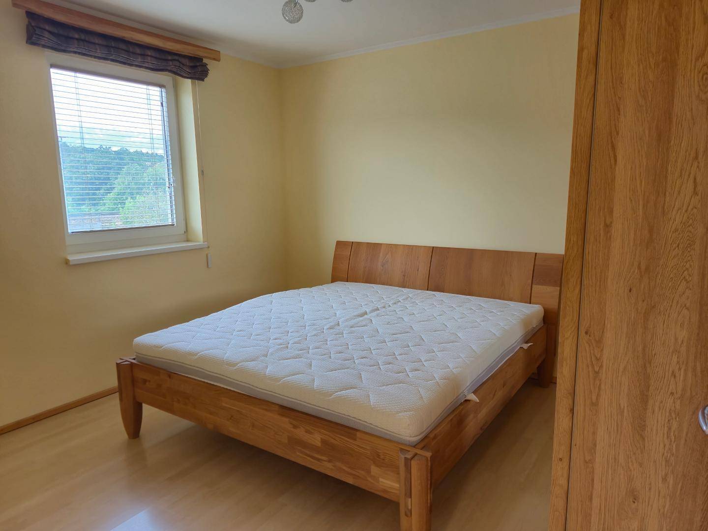 Schlafzimmer mit hellem Holzbett, Parkettboden und Fenster mit Blick ins Grüne.
