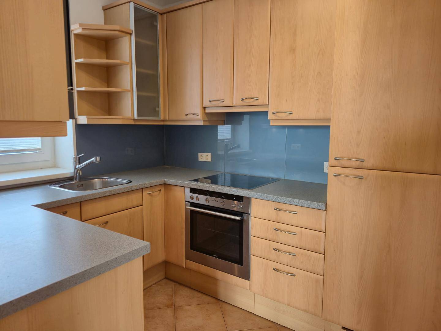 Einbauküche mit Holzfronten, grauer Arbeitsplatte, integriertem Backofen und Induktionskochfeld.