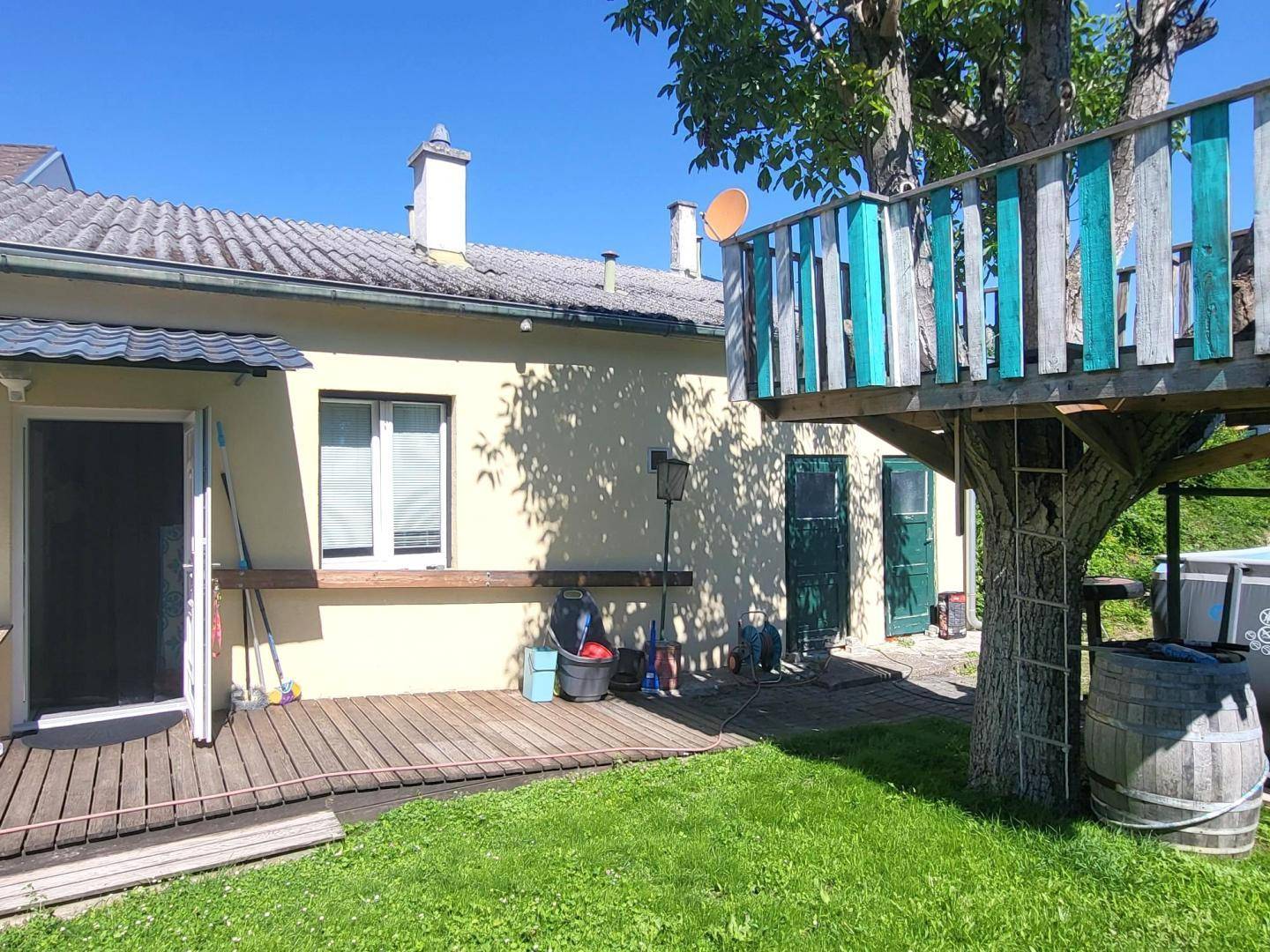 Außenansicht des Hauses mit Holzterrasse und einem charmanten Baumhaus im Garten.
