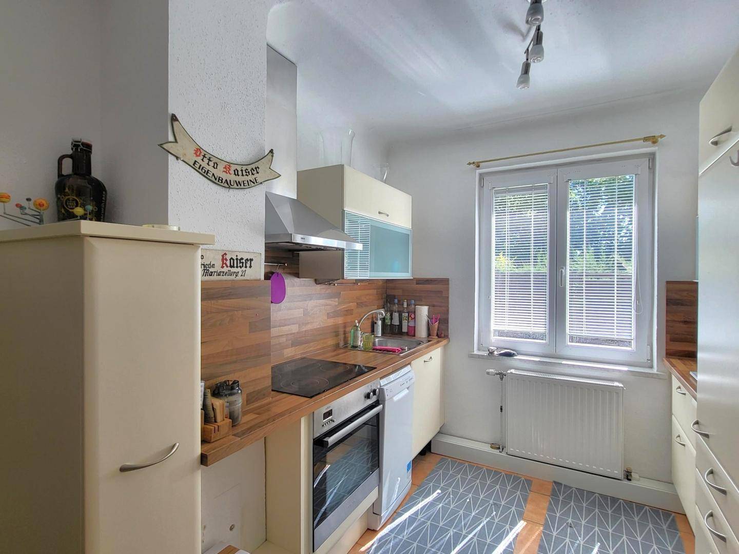 Funktionale Küche mit beigen Schränken, Holzarbeitsplatten und einem Fenster mit Blick ins Grüne.