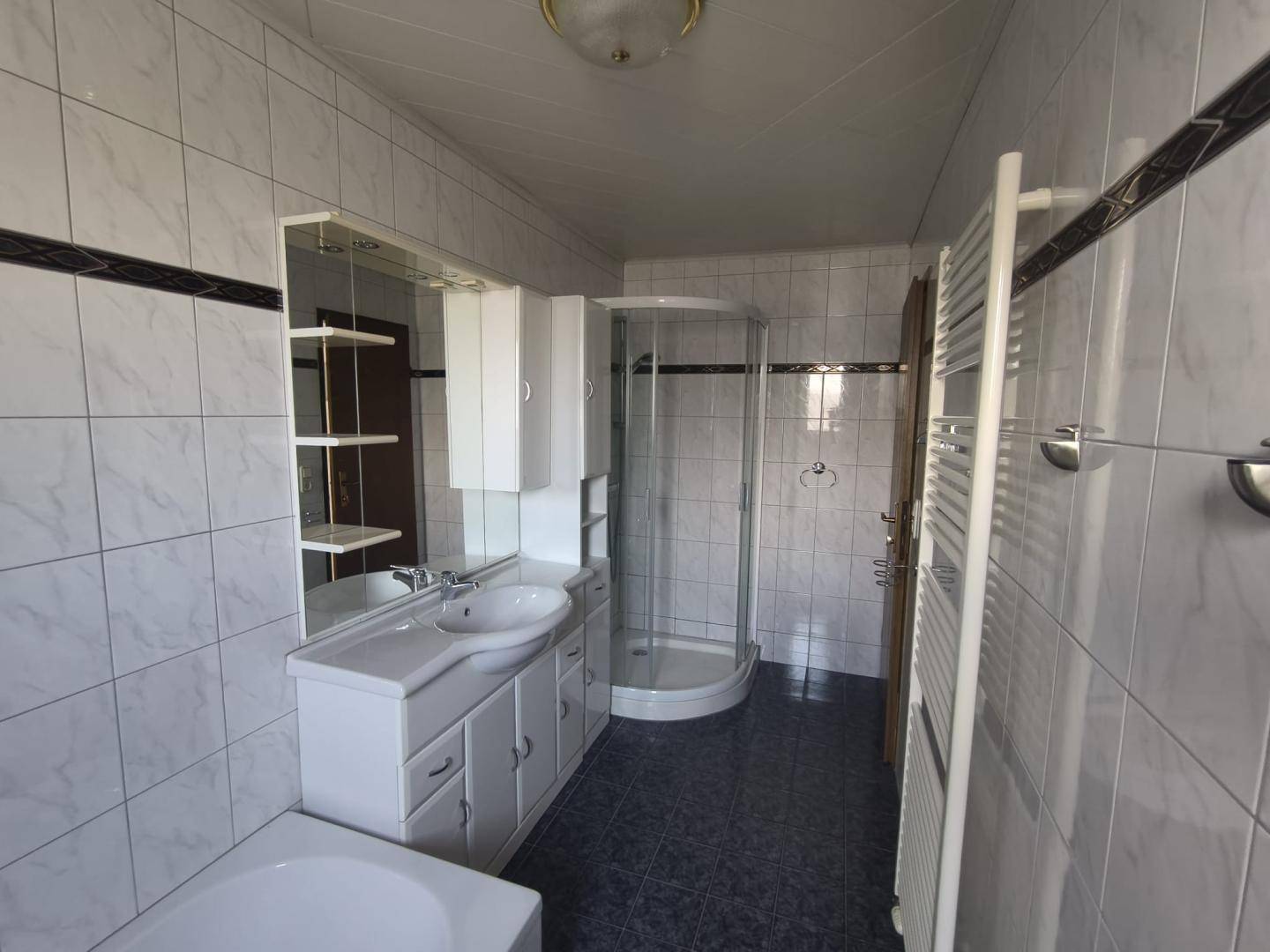 Gefliestes Badezimmer mit Dusche, Badewanne, Einzelwaschbecken und Handtuchheizkörper.