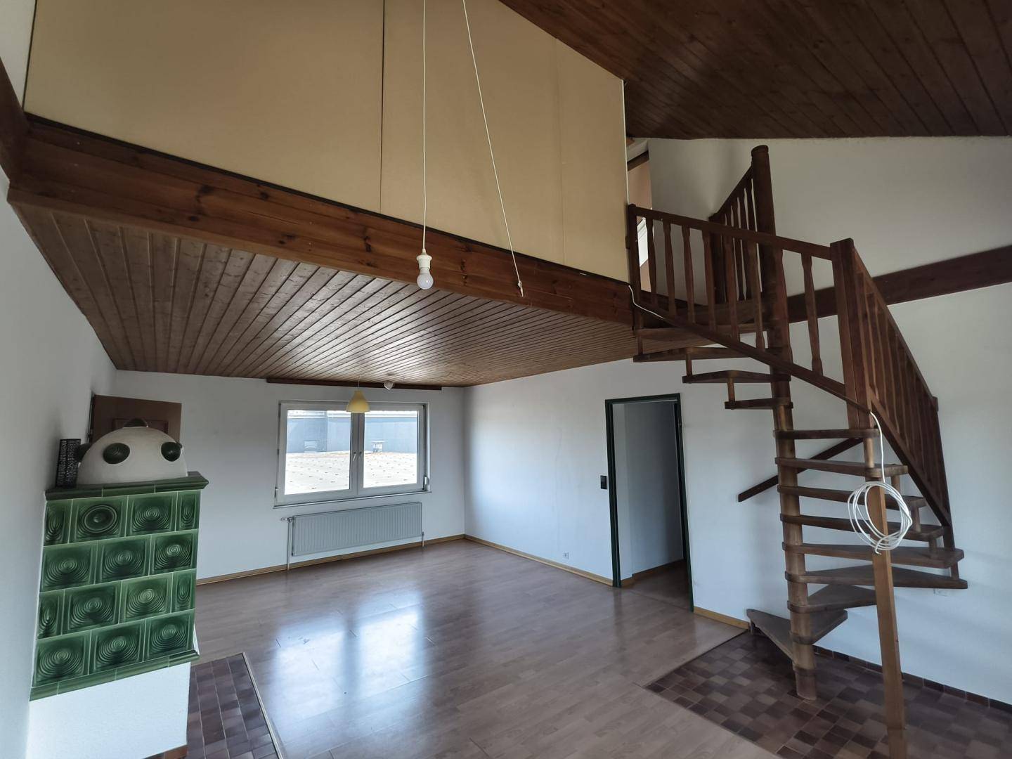 Geräumiger Wohnbereich mit hoher Holzdecke, Wendeltreppe und Kachelofen.