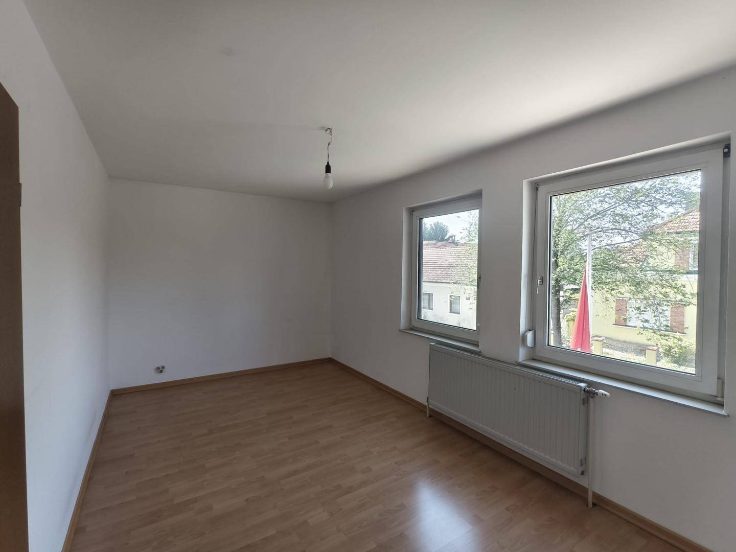 Helles Zimmer mit Laminatboden und zwei Fenstern, ideal als Schlaf- oder Arbeitszimmer.