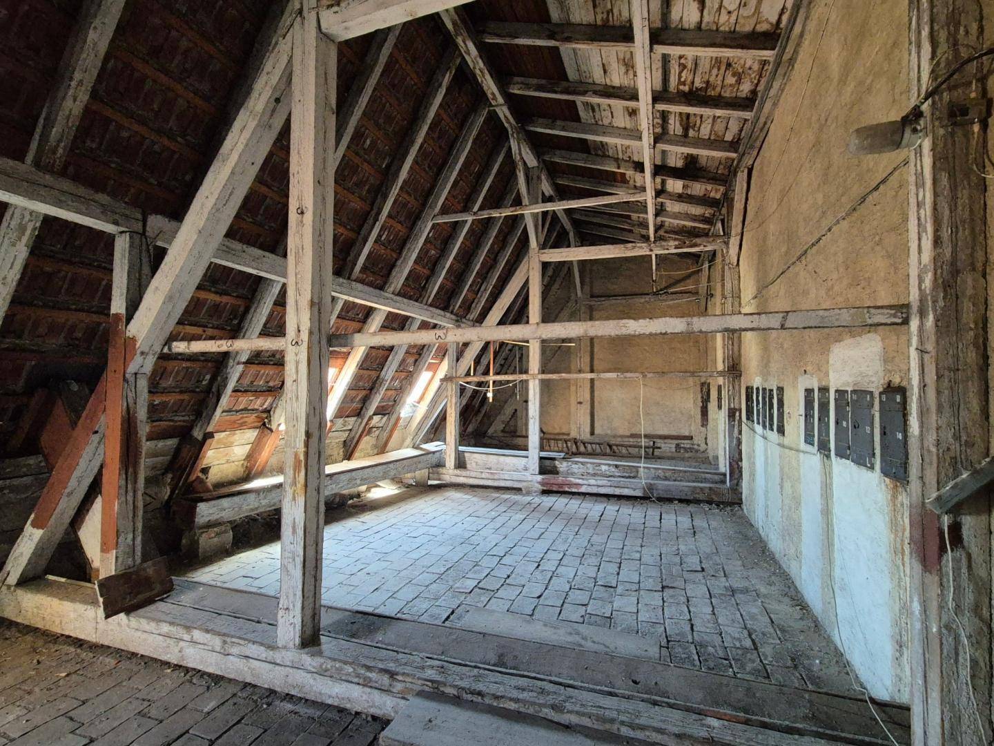 Geräumiger Dachboden mit freiliegenden Holzbalken und rustikalem Ziegelboden, bereit zum Ausbau.