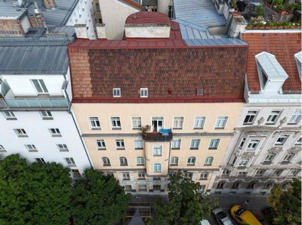 Luftaufnahme des Gebäudes mit rotem Dach und einem kleinen Balkon, umgeben von anderen Stadtgebäuden.
