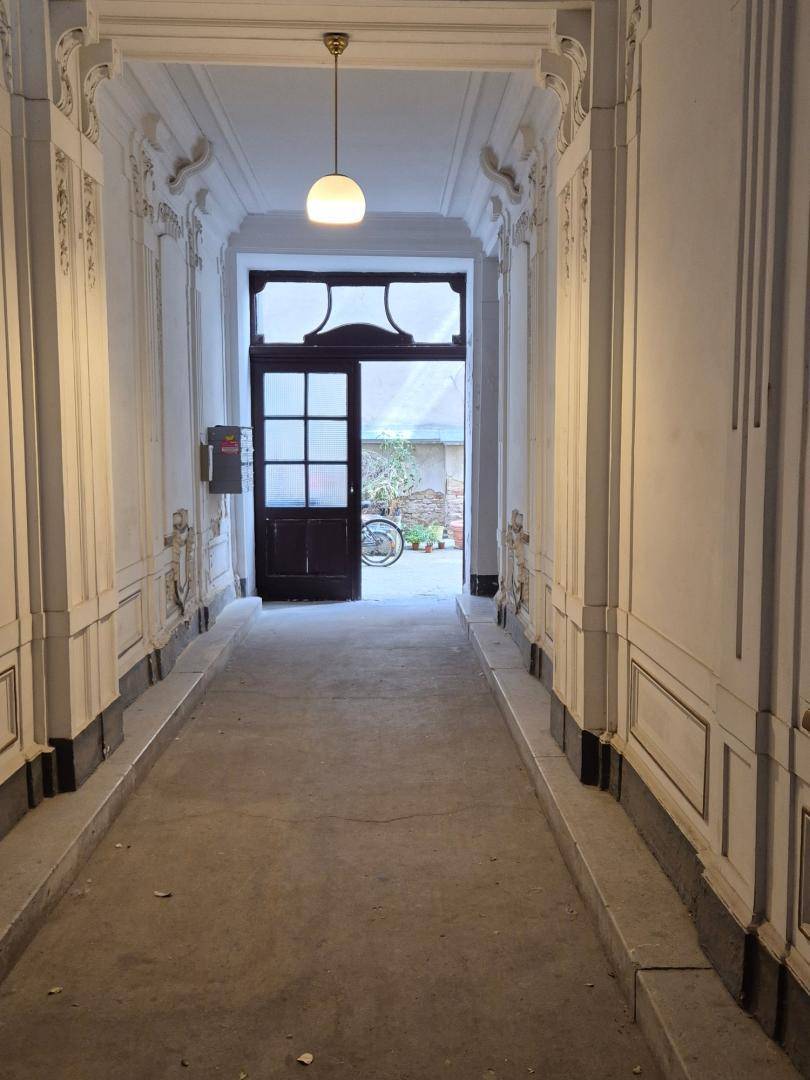 Langer, eleganter Flur mit Stuckverzierungen und einer Tür, die zu einem Innenhof führt.