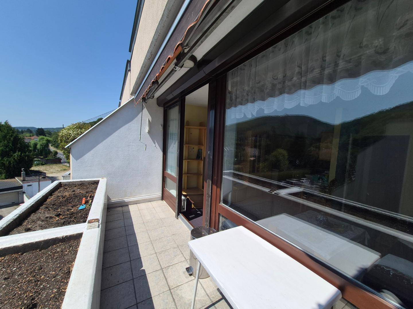 Sonniger Balkon mit Fliesenboden, Pflanzkästen und Zugang zu einem Innenraum.