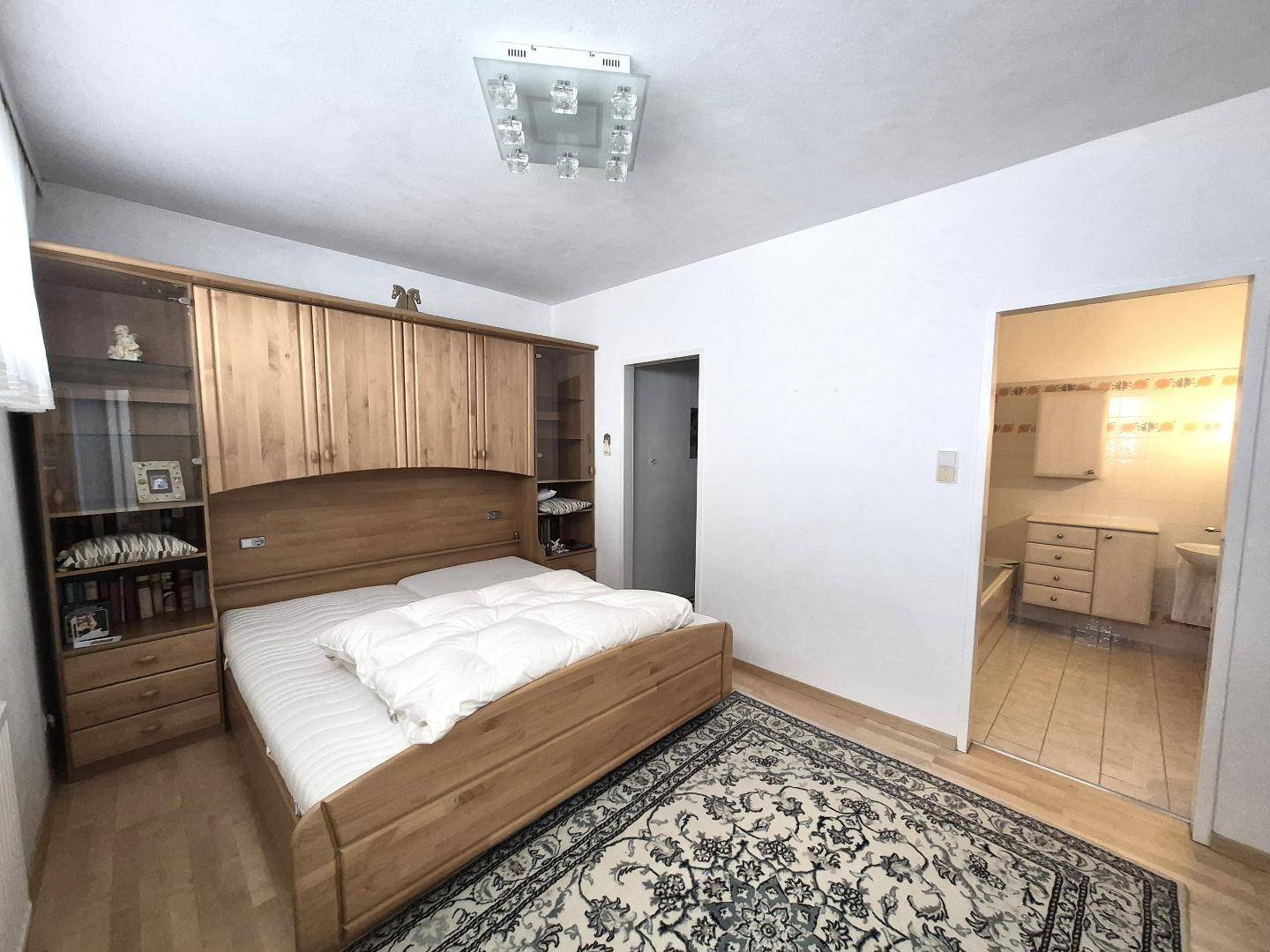 Schlafzimmer mit Holzdoppelbett, Einbauschränken und Teppichboden, mit Zugang zum Badezimmer.