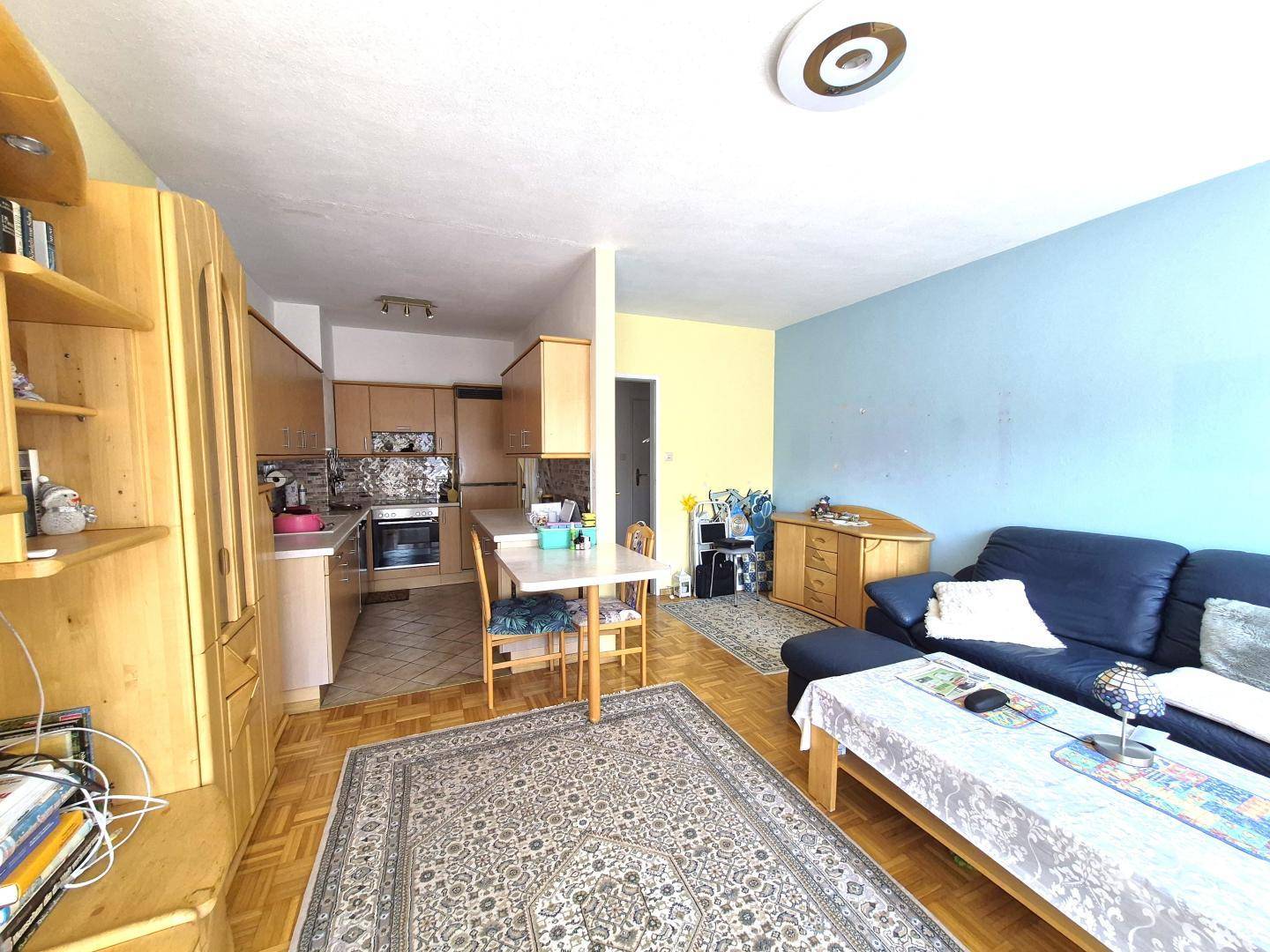Offener Wohnbereich mit Sofa und Essplatz, angrenzend an eine Küche mit Holzmöbeln.