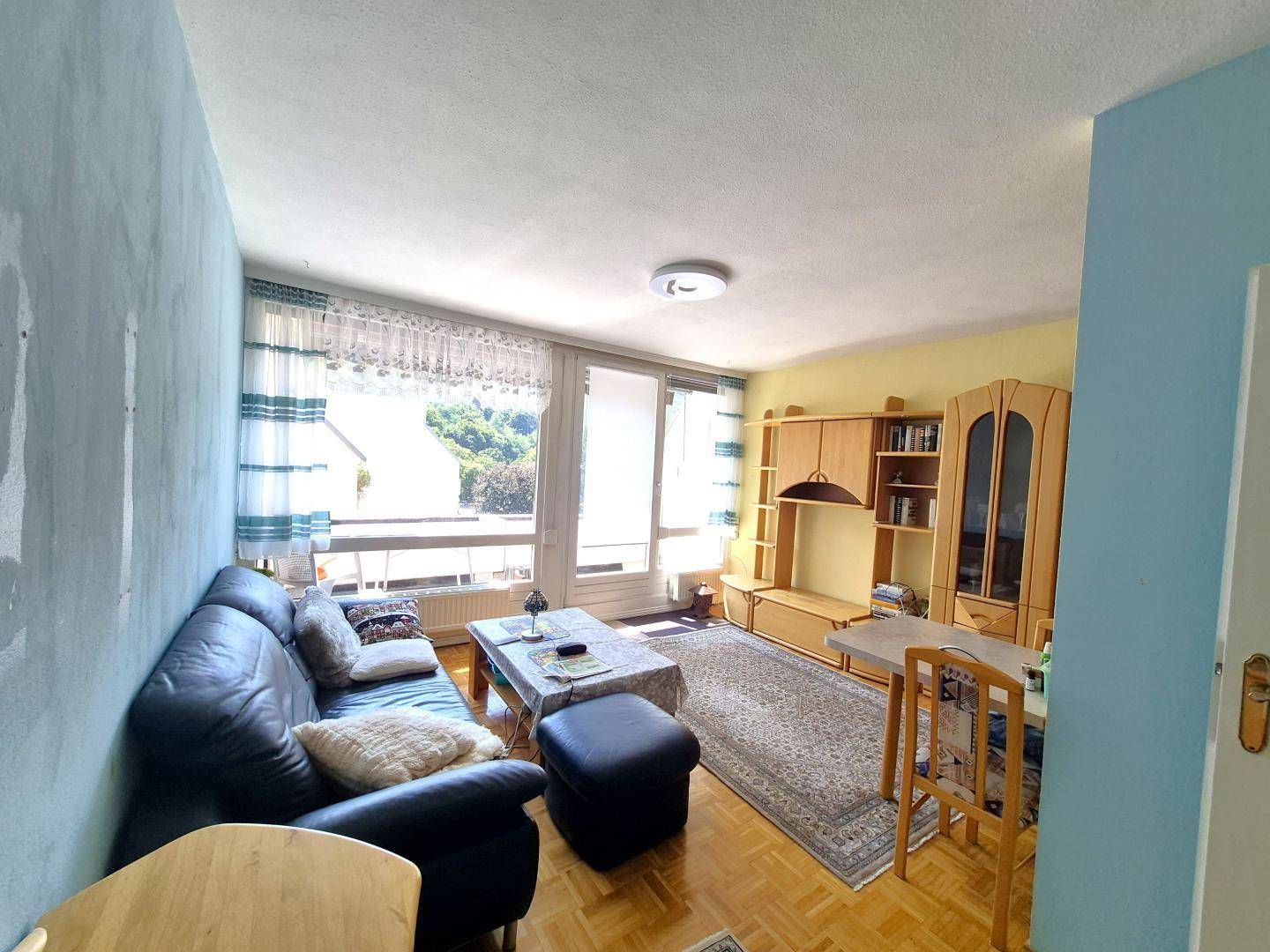 Gemütliches Wohnzimmer mit dunklem Sofa, Holzmöbeln, Parkettboden und Zugang zum Balkon.
