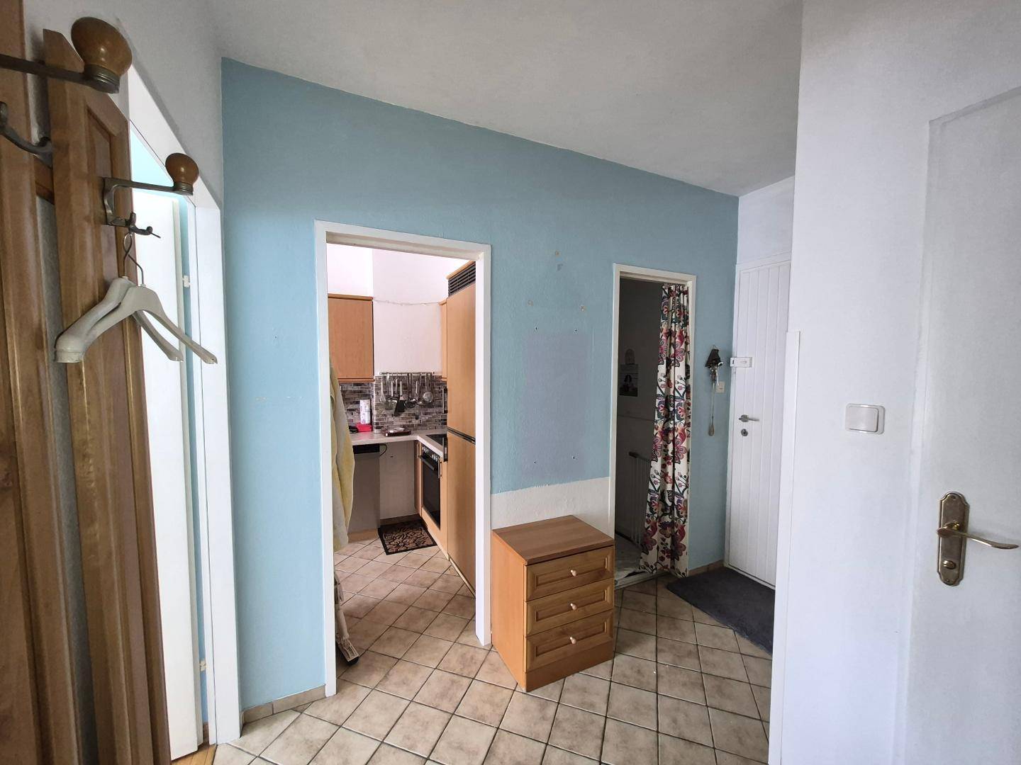 Heller Flur mit Fliesenboden und blauen Wänden, verbindet verschiedene Räume der Wohnung.