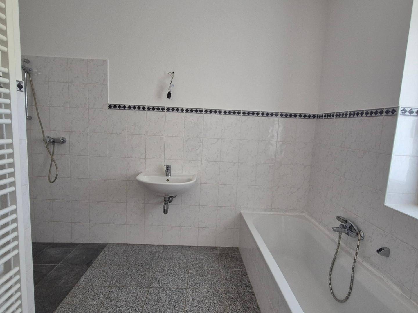 Badezimmer mit weißen Fliesen, Badewanne, Dusche und beheiztem Handtuchhalter.