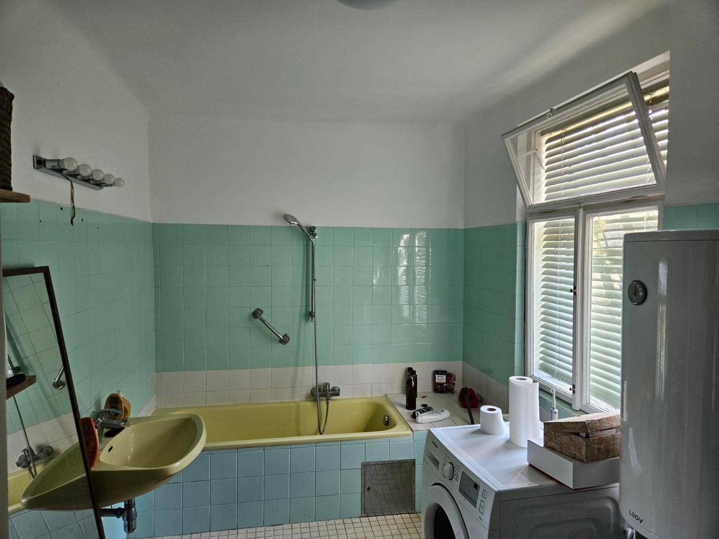 Badezimmer im Stil der 80er Jahre mit mintgrünen Fliesen, Badewanne und Waschmaschine.