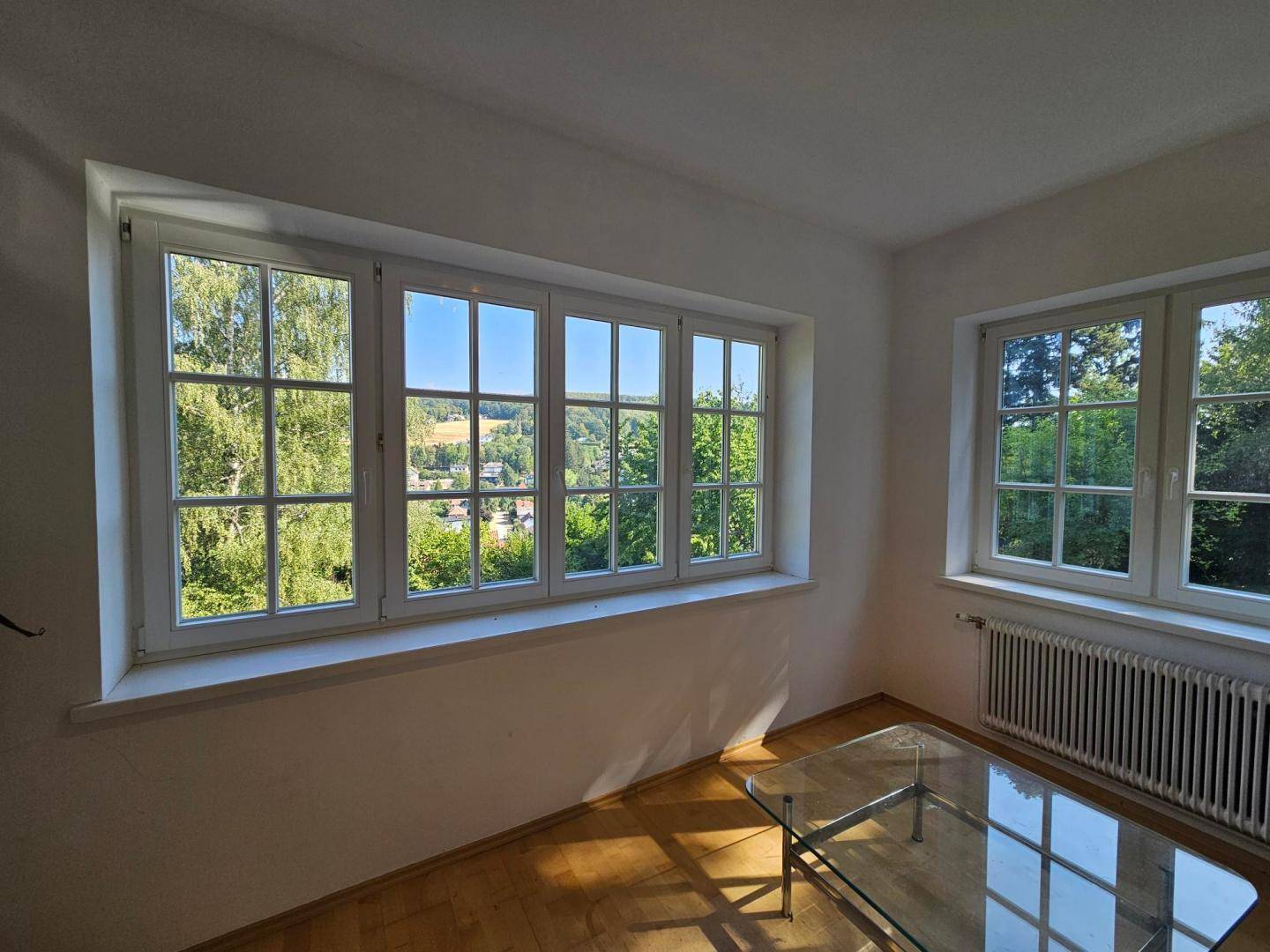 Heller Raum mit großen Sprossenfenstern, die einen weiten Blick ins Grüne bieten.