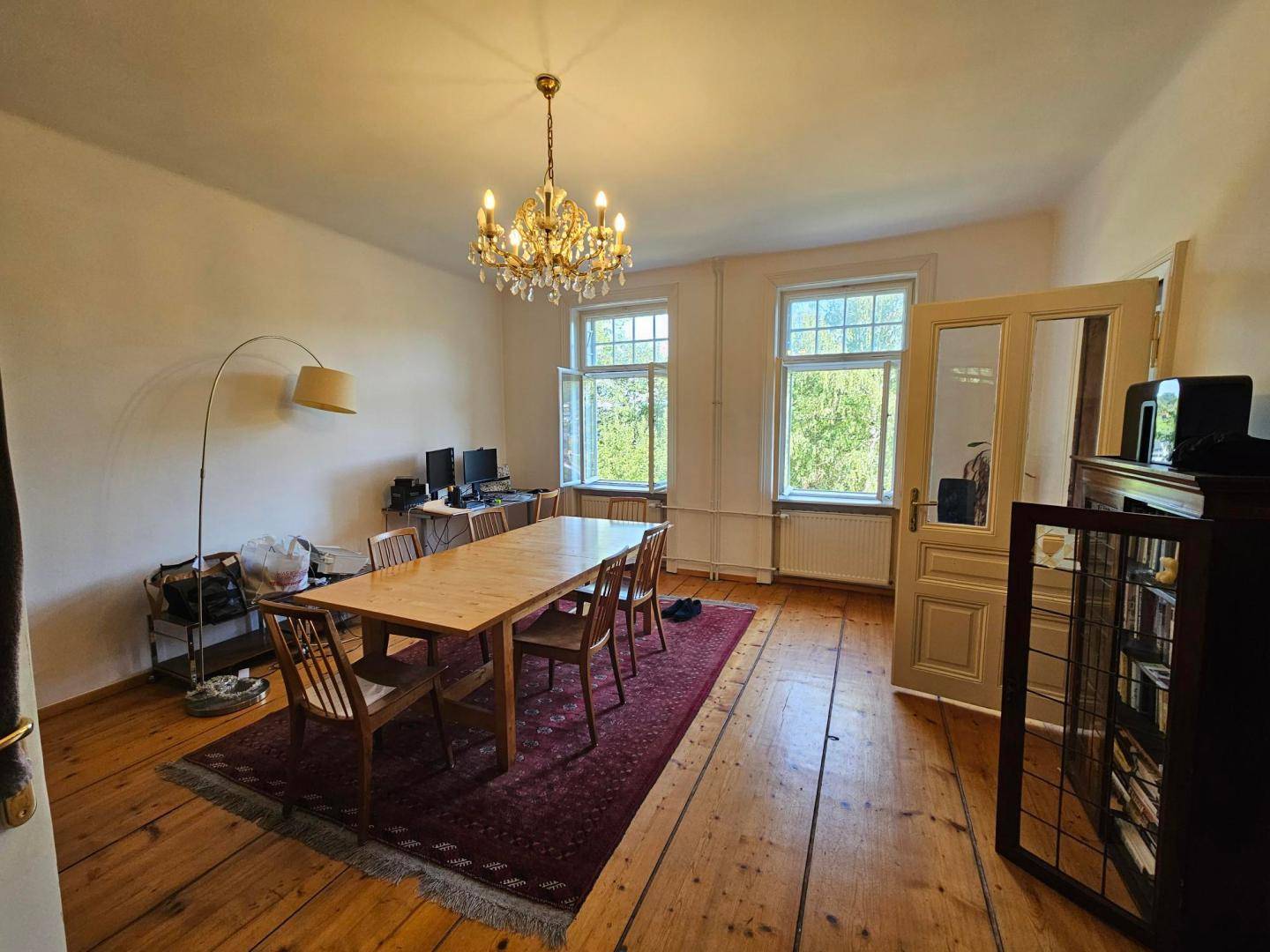 Geräumiges Esszimmer mit Holzdielenboden, Kronleuchter und einem großen Holztisch.