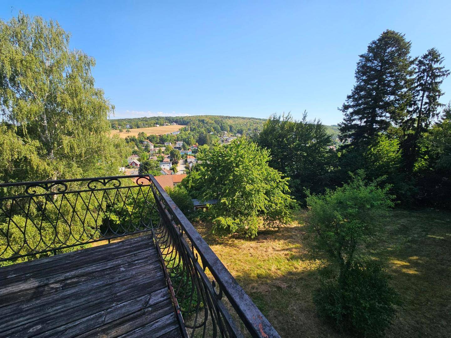 Alter Balkon mit schmiedeeisernem Geländer und weitem Blick über die grüne Landschaft.